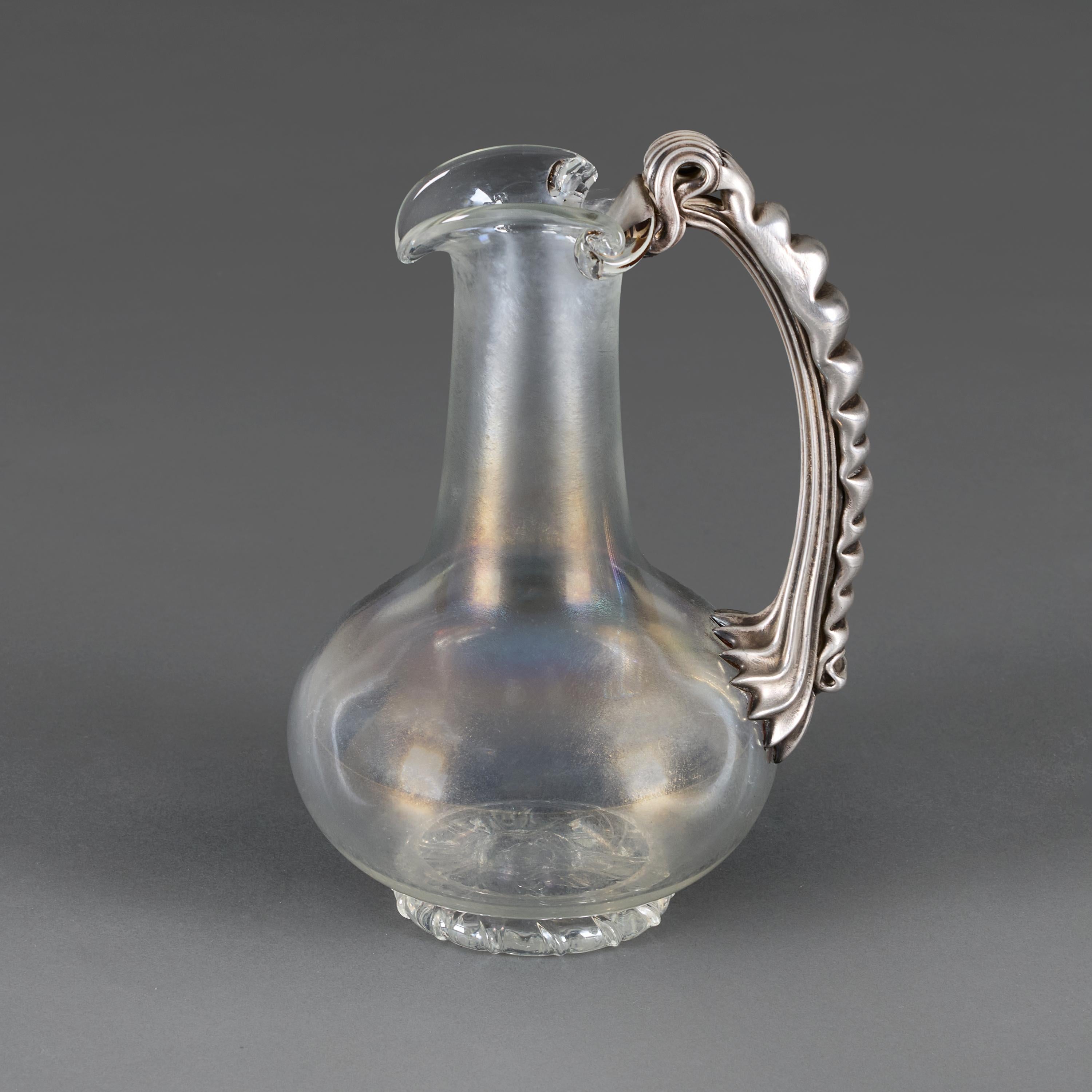 Czech Republic, circa 1880

A late nineteenth century Bohemian glass water jug, the iridescent body supported on a circular base with a hot-applied silver gilt handle, in the manner of Harrach.  

Height   26.00cm
Width   18.00cm
Depth  15.00cm