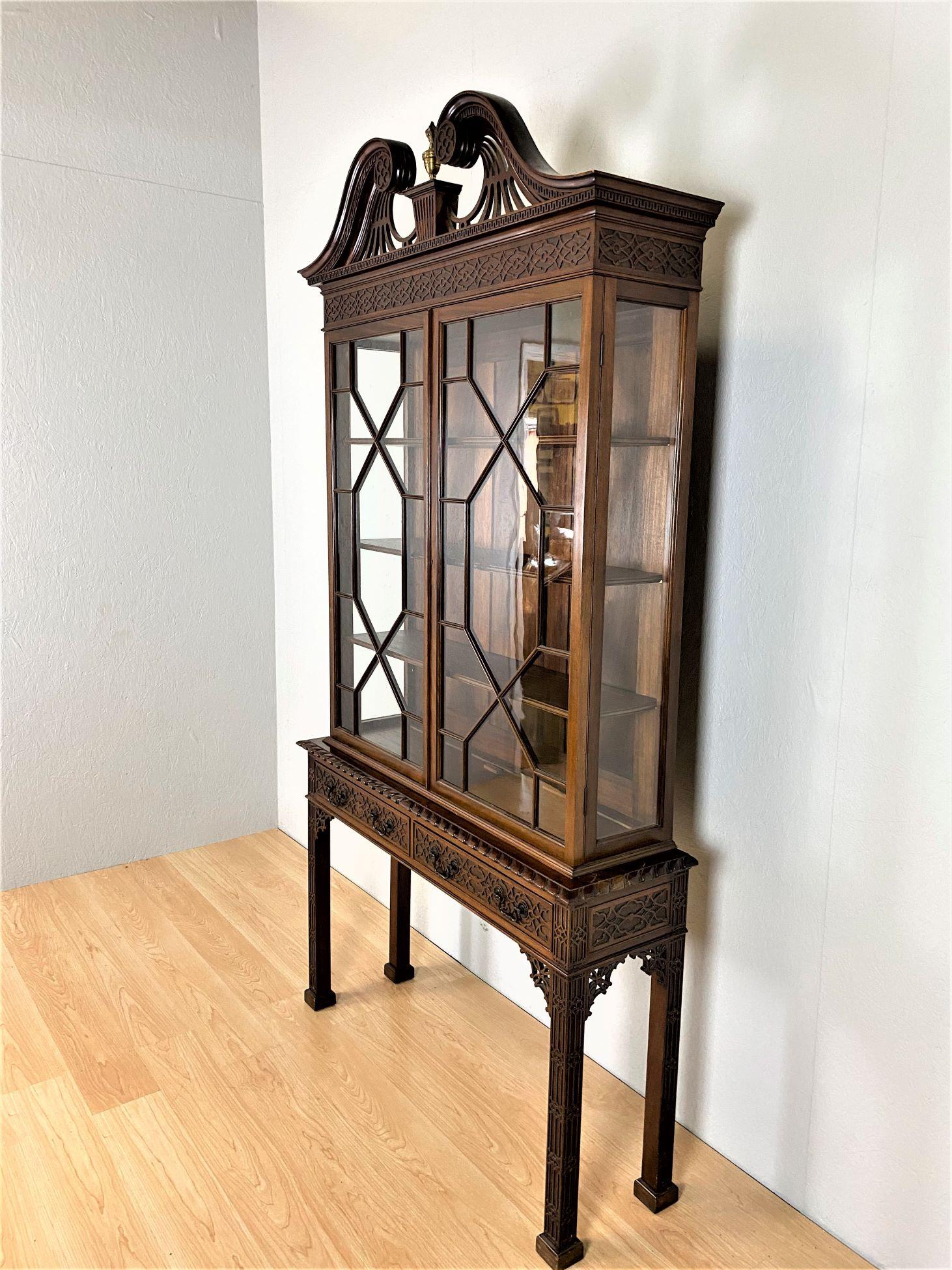 A fine late 19th century mahogany display cabinet in the Chippendale style.
The swan-neck pierced broken arch pediment with a central brass finial, sits above a pair of astragal glazed doors with a pair of blind fretwork fronted drawers with iron