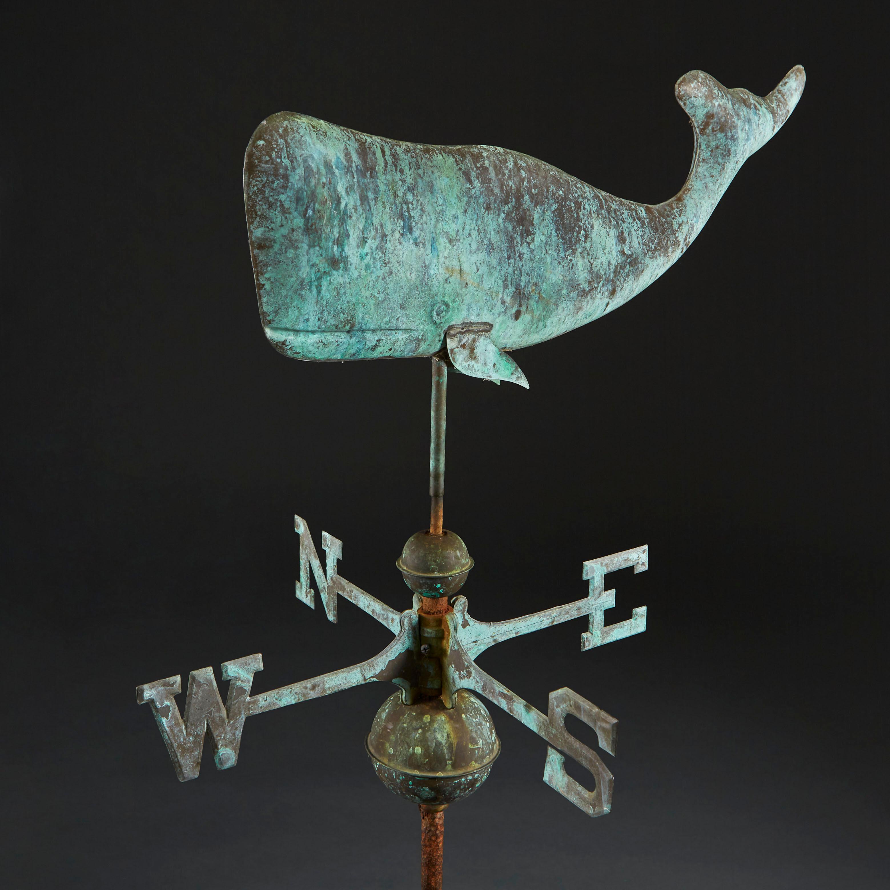 An unusual and charming verdigris weather vane with a sperm whale to the top, currently mounted on a wooden base.

Suitable for mounting on the rood of a building.