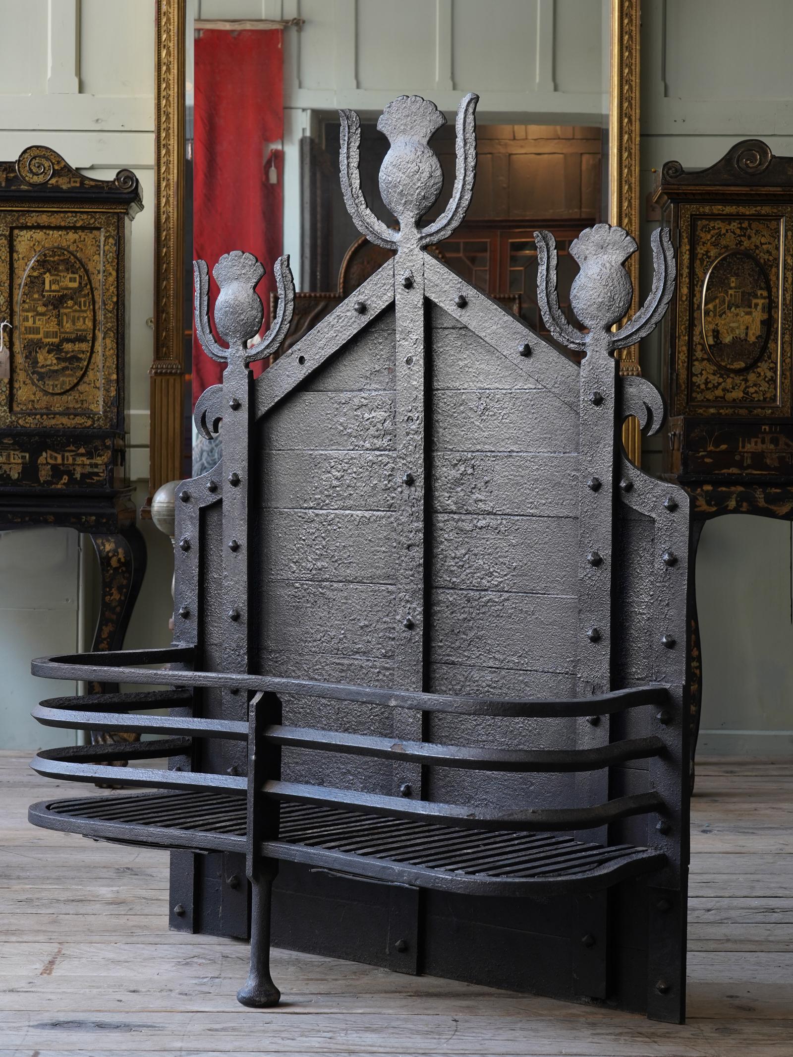 The serpentine railed basket with central support, the tall sectional fire back is surmounted by three Scottish thistle motifs. 

By repute these grates were retailed by Liberty of London.
    