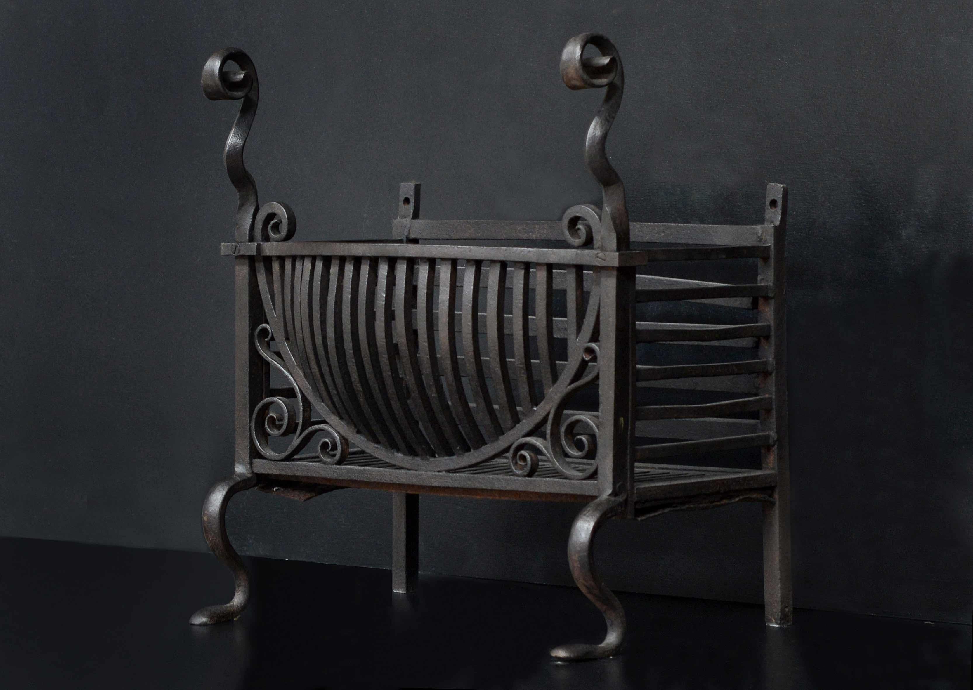 A late 19th century English wrought iron firegrate. The bowl front with vertical front bars, flanked by scrollwork and surmounted by scrolled finials. Scrolled feet below. Plain cast iron back behind.

Width At Front:	507 mm      	20