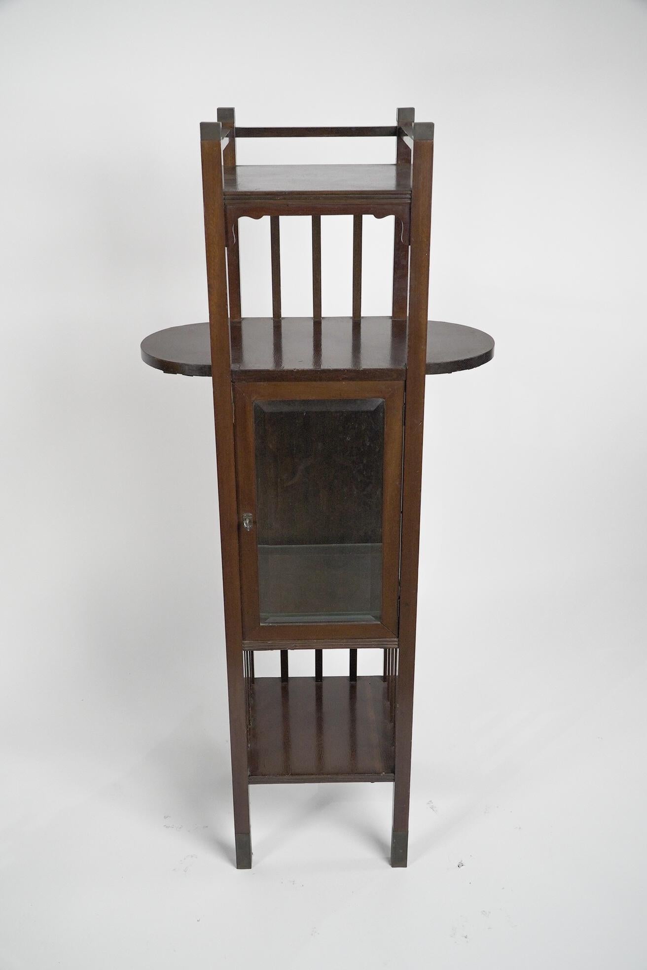 An Anglo-Japanese style Mahogany side cabinet of slender form with upper extending display wings, a beveled glass door, and glass sides, a sign of good quality, standing on brass sabot feet.
