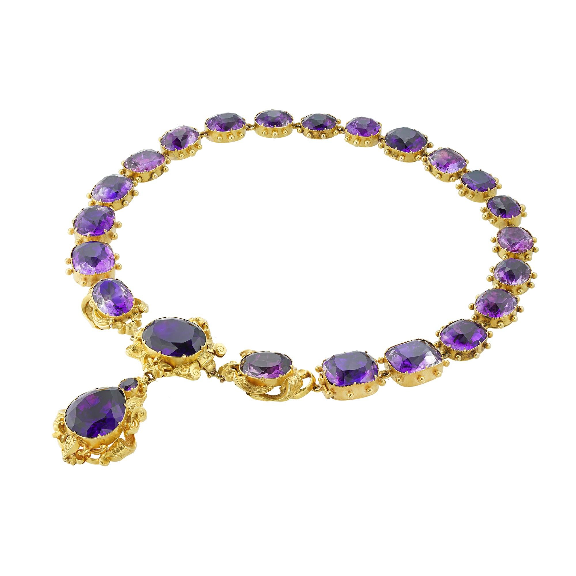 A late Georgian amethyst suite, the necklace centrally set with three oval faceted amethysts within gold scroll decorations, suspending a detachable drop with a pear-shaped and a small oval amethyst on a similar surround, attached to nineteen