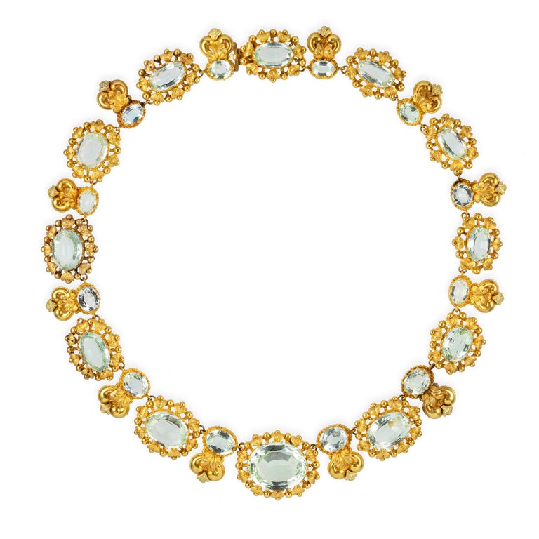 A late Georgian gold aquamarine parure of a necklace, a pair of drop earrings, a bodice brooch, a brooch, a hair ornament and a stick pin, the collar necklace with graduating oval-cut aquamarines from 11ct to 2ct, each surrounded by gold foliate
