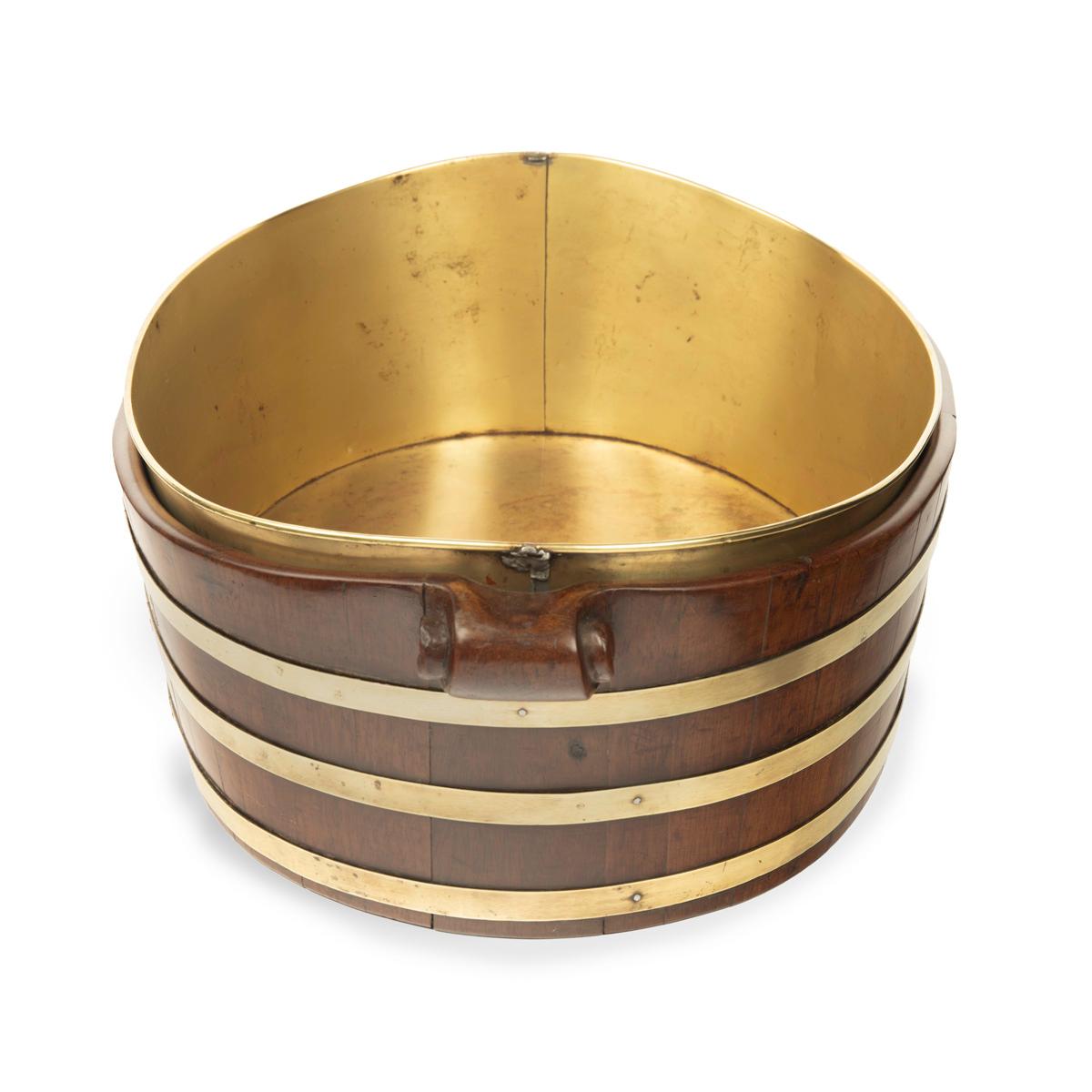 A late Georgian brass bound mahogany oyster bucket, of oval form with three brass bands, wooden volute handles and the original brass liner.  English, 1810.