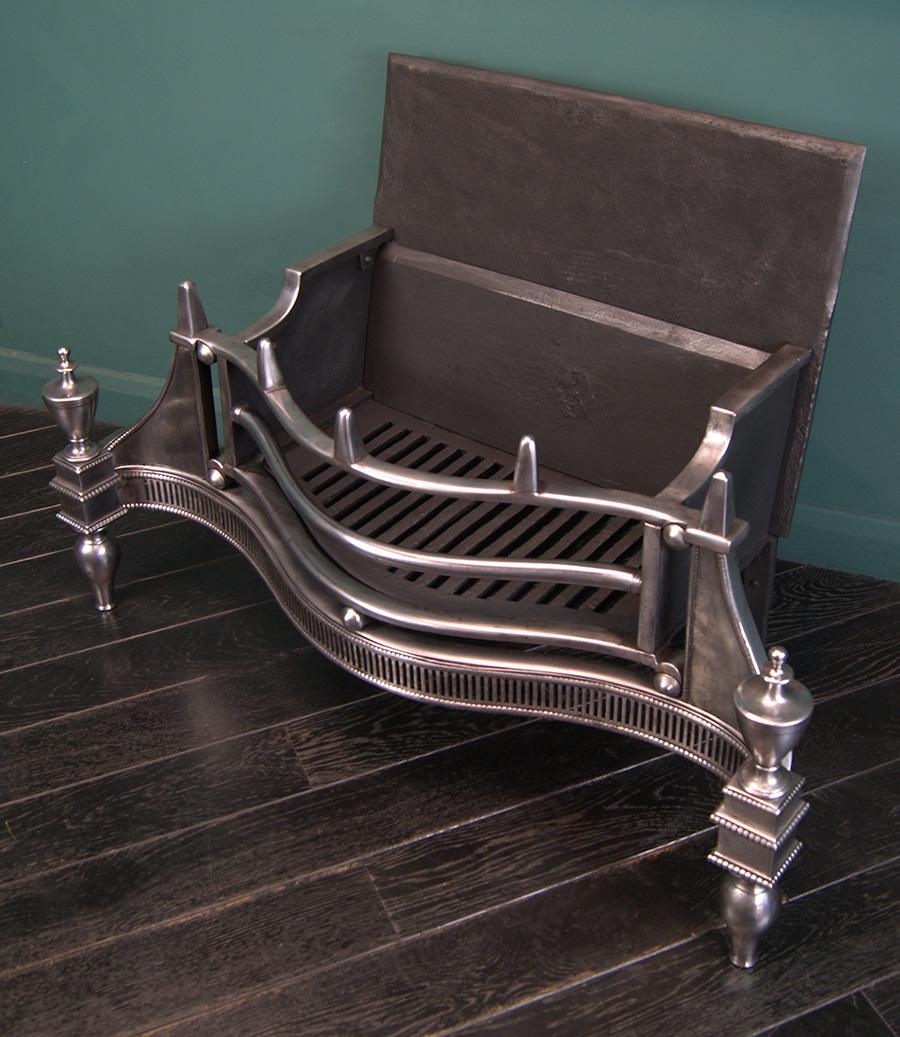 A late Georgian large polished steel fire grate of serpentine form with fire bars set over steel ball detail and pinnacle finials uppermost. The fluted fret, urn mounts and wings all lined with beaded moulding set in front of a bevel10ed fire back.