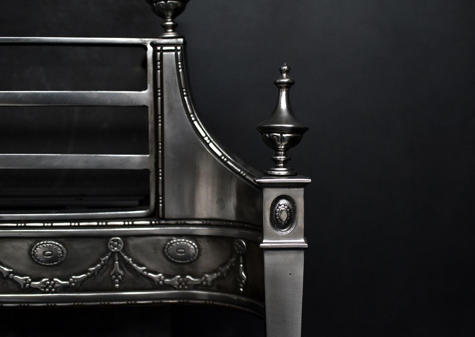 A George III style polished steel firegrate. The tapering legs surmounted by urn finials, the fret with swags and paterae throughout, with sausage-and-pea beading above and below. Plain cast iron fireback behind. English, circa 1900.

Width At