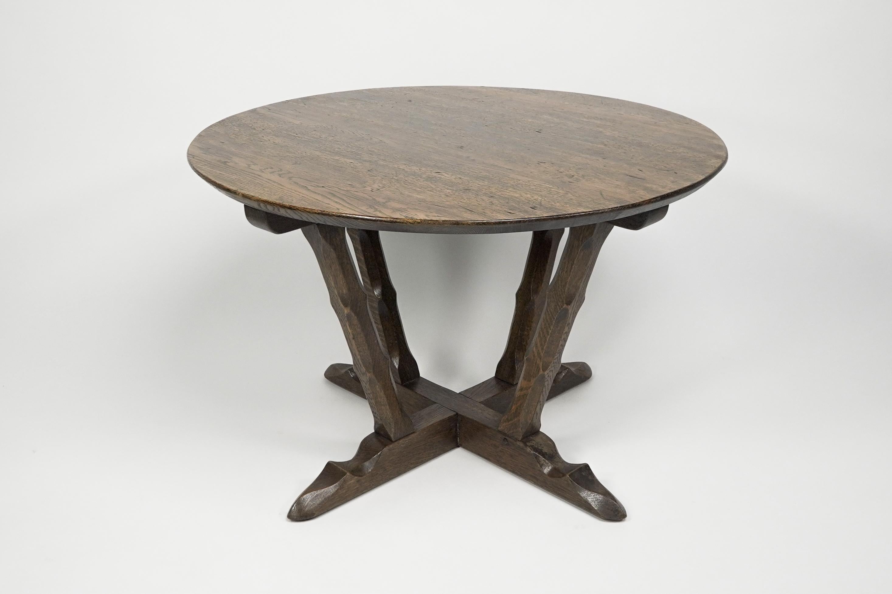 A late Arts and Crafts oak circular coffee table with deep sculptured chamfered details raised on angular legs that united to a cross stretcher footed base. 
Made by Rupert Griffiths of the Monastic Woodcraft Furniture Company.