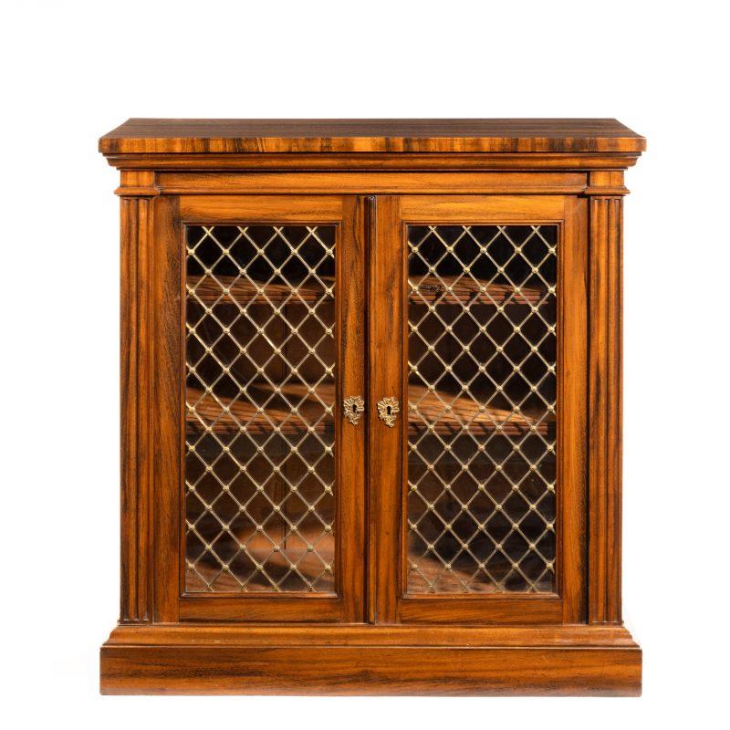 A late Regency Gonçalo Alves two-door side cabinet firmly attributed to Gillows, of rectangular form with two glazed doors retaining the original brass trelliswork centred on rosettes, flanked by fluted pilasters, enclosing two adjustable shelves,