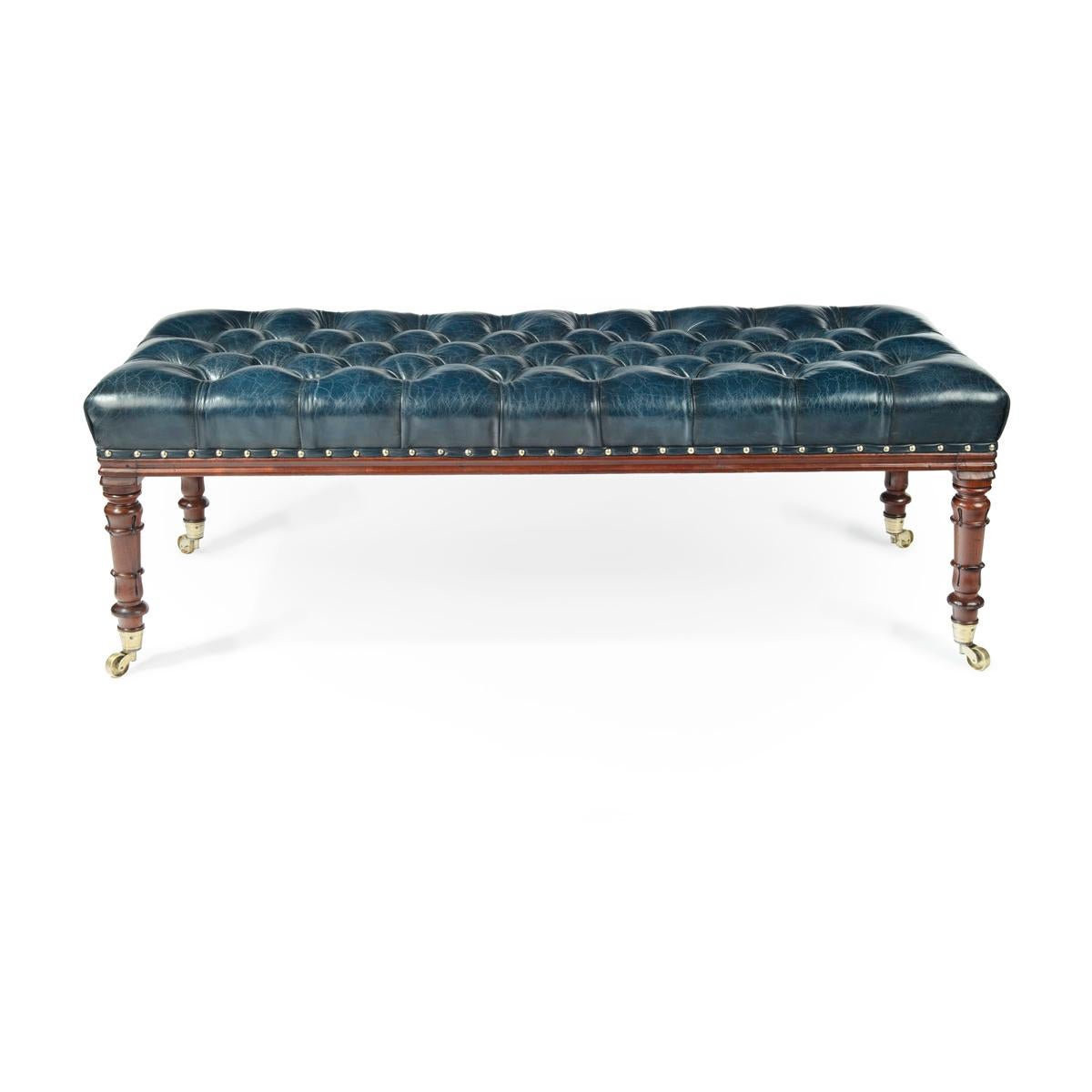 A late Regency Rosewood stool, of long rectangular form, the turned tapering legs terminating in the original brass castors, reupholstered in deep buttoned blue leather.   English, circa 1815.

