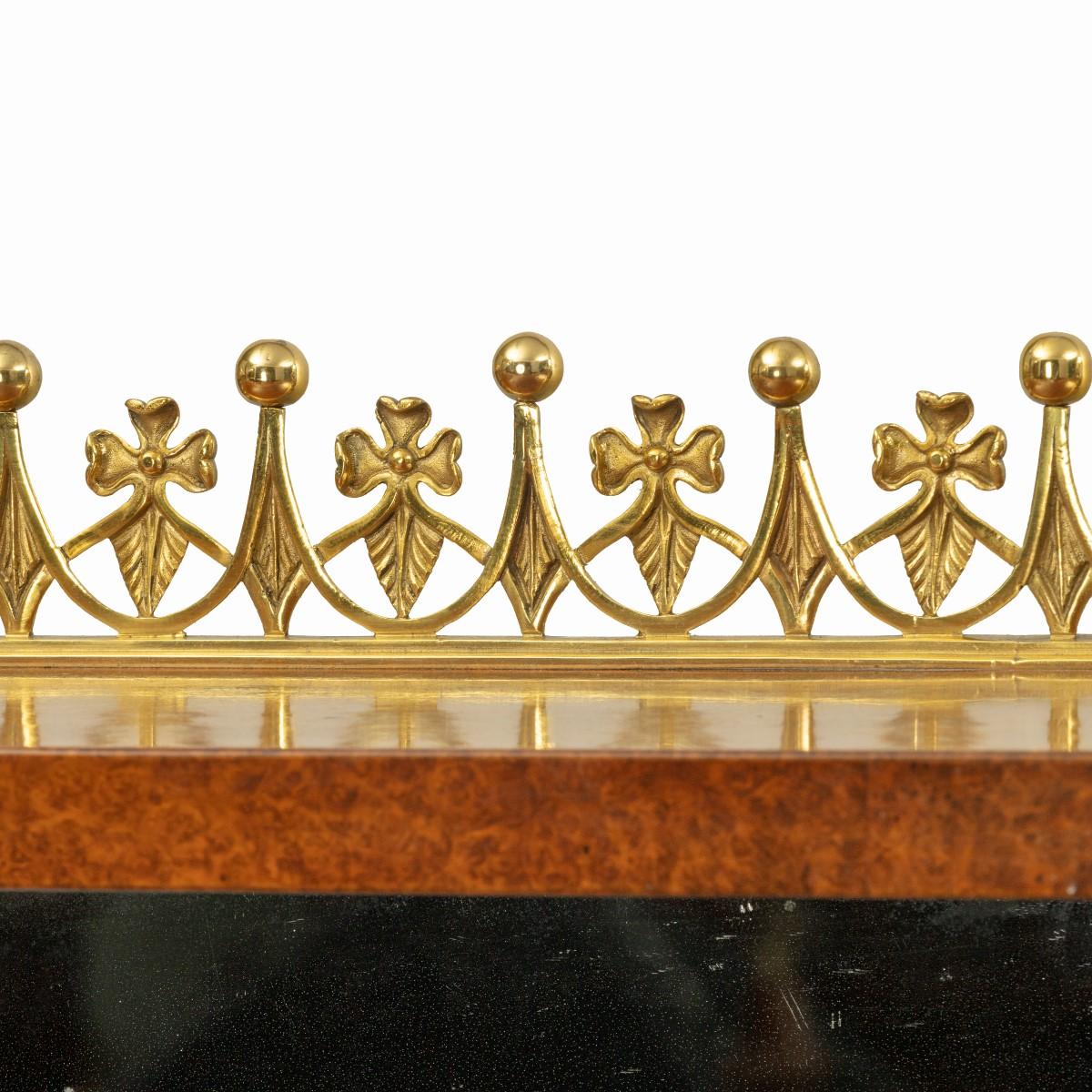 Un meuble d'appoint en amboine de la fin de la Régence, à base rectangulaire avec deux armoires vitrées élancées, flanquées de colonnes en ébène avec des montures en bronze doré, de part et d'autre d'une plinthe centrale à fond de miroir, le plateau