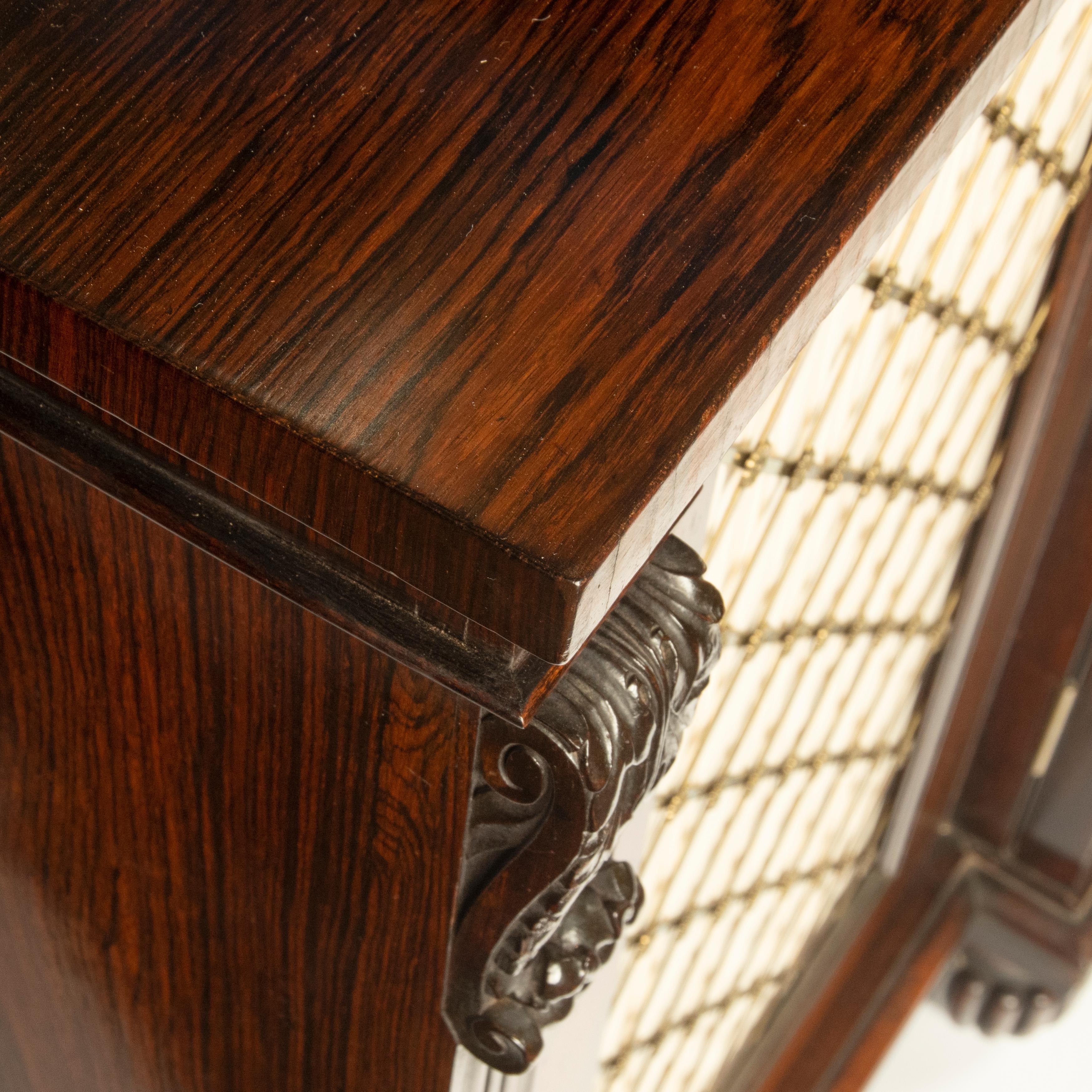 A late Regency rosewood breakfront four door side cabinet, attributed to Gillows, the shaped top with a brass gallery above four doors fitted with trellis-and-rosette grilles relined in silk, divided by four fluted pilasters decorated with scrolling