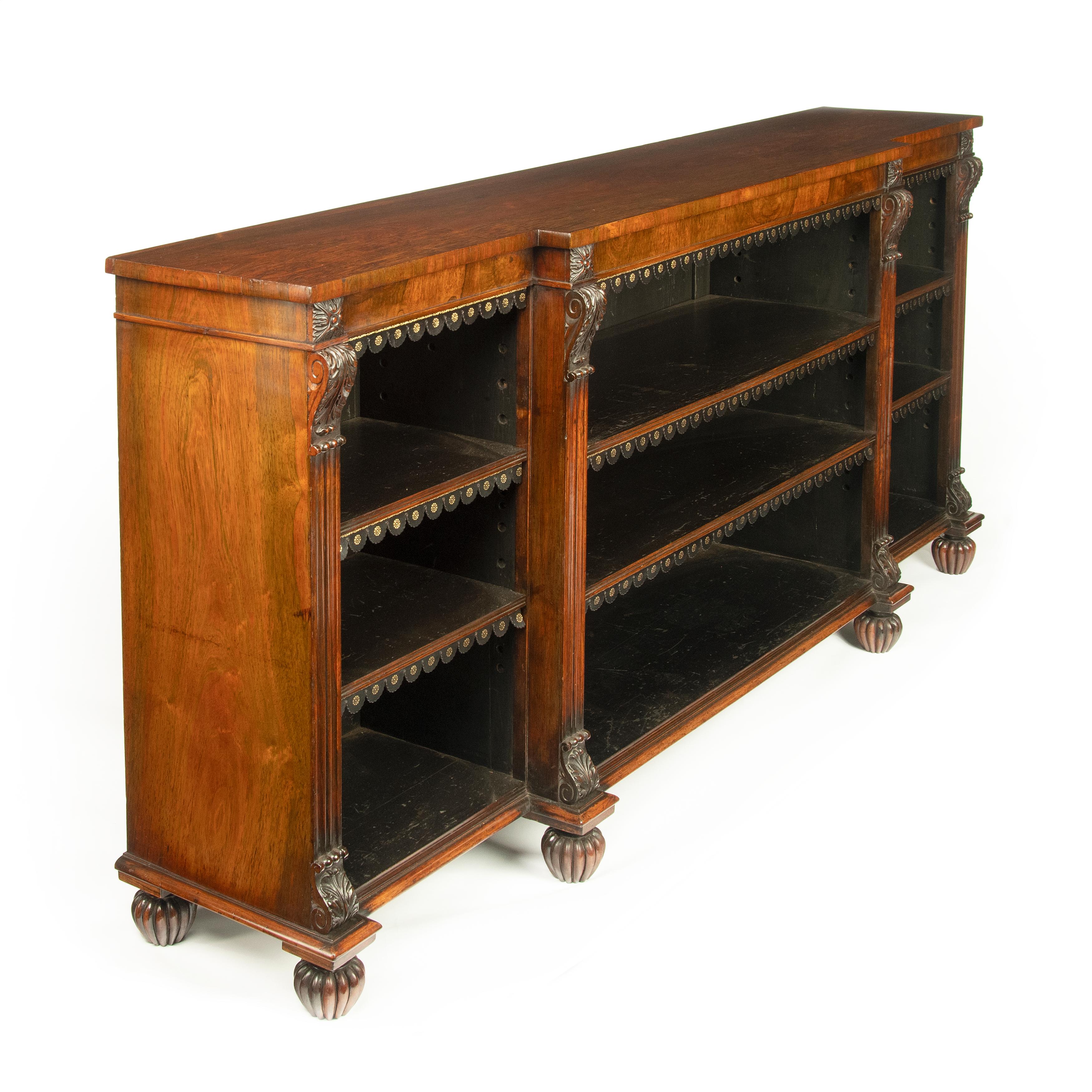 A late Regency rosewood breakfront open bookcase, attributed to Gillows, of rectangular form with three adjustable shelves, with tooled leather dust fringes, divided by four fluted pilasters decorated with scrolling corbels and acanthus carved