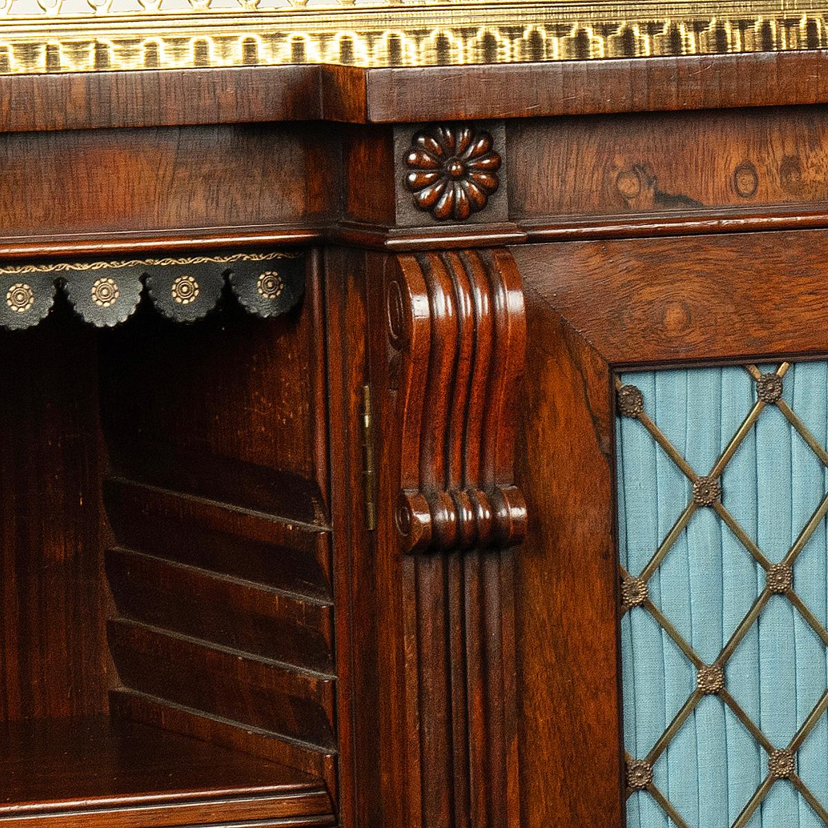 A late Regency rosewood breakfront side cabinet attributed to Gillows, of long rectangular form with an ormolu gallery a two central doors flanked by adjustable shelves within reeded pilasters with scroll corbels, the shelves with later leather dust