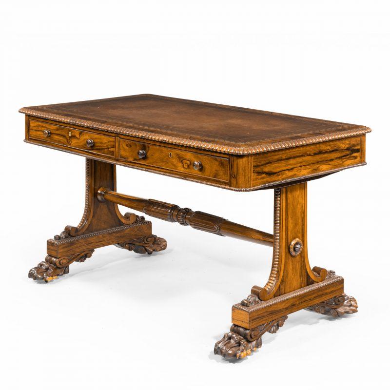 A late Regency rosewood free standing library table, by James Winter, the rectangular leather-inset top with a gadrooned edge and frieze enclosing two drawers on one side and two corresponding dummy drawers on the other, the solid end supports with