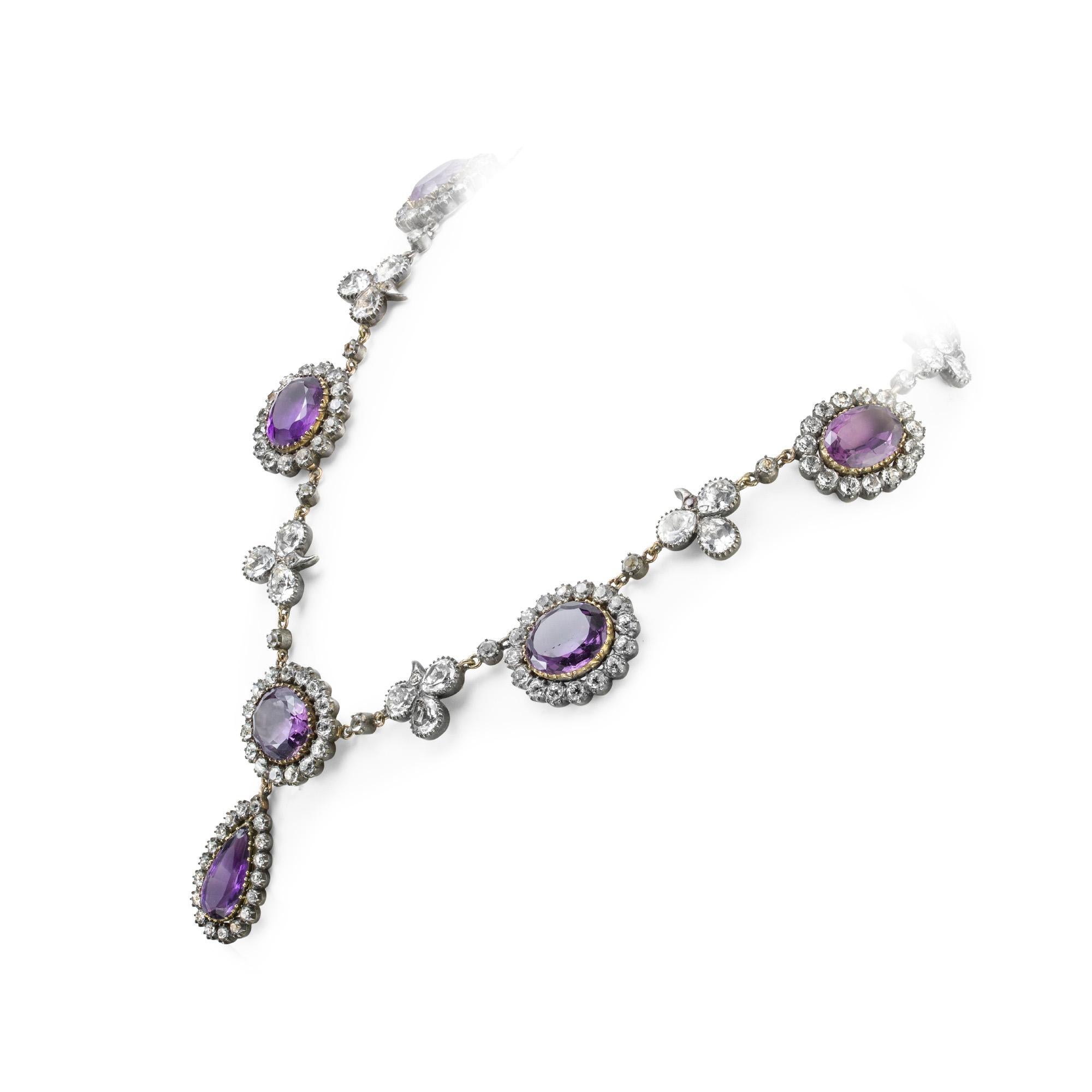 A late Victorian amethyst and rock crystal necklace, the seven oval-shaped amethysts surrounded by a cluster of round-cut rock crystal set in silver to yellow gold, each cluster separated with a rock crystal folitate trefoil, the centre cluster