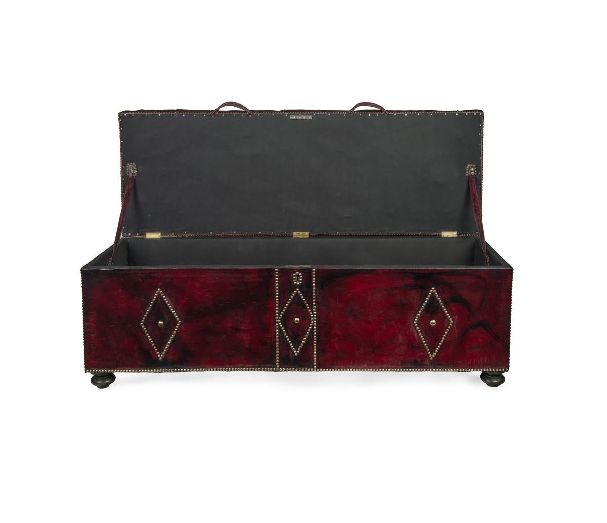 A late Victorian box ottoman, of rectangular form re-upholstered overall in distressed burgundy leather, the hinged lid deep-buttoned to form a seat, the sides decorated with close-nailed brass lozenges and edging, on turned feet.  English, circa