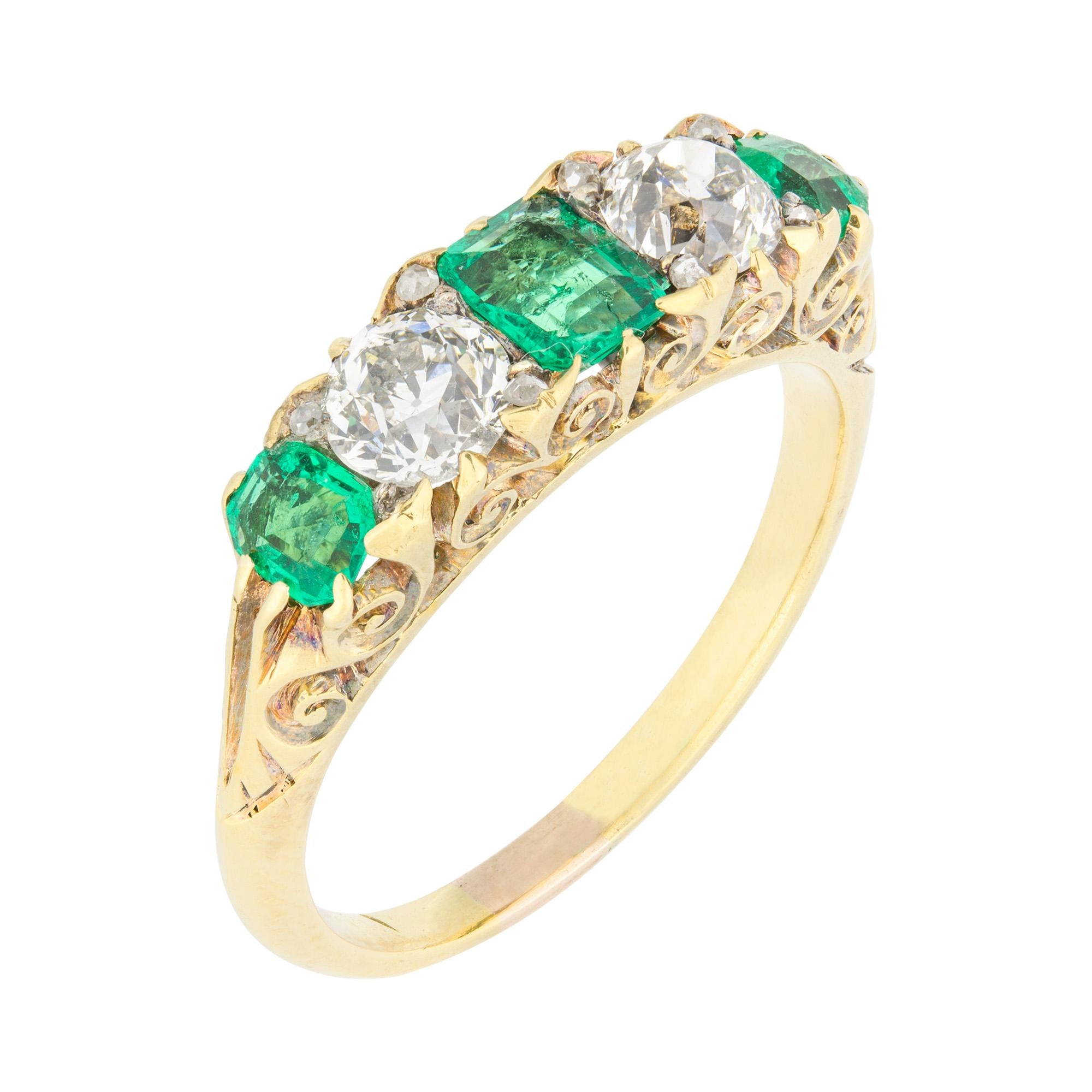 A late Victorian emerald and diamond carved half hoop ring, the three graduating emerald-cut emeralds, estimated to weigh a total of 0.6 carats, and two old brilliant-cut diamonds, estimated to weigh a total of 0.6 carats, with rose-cut diamonds set