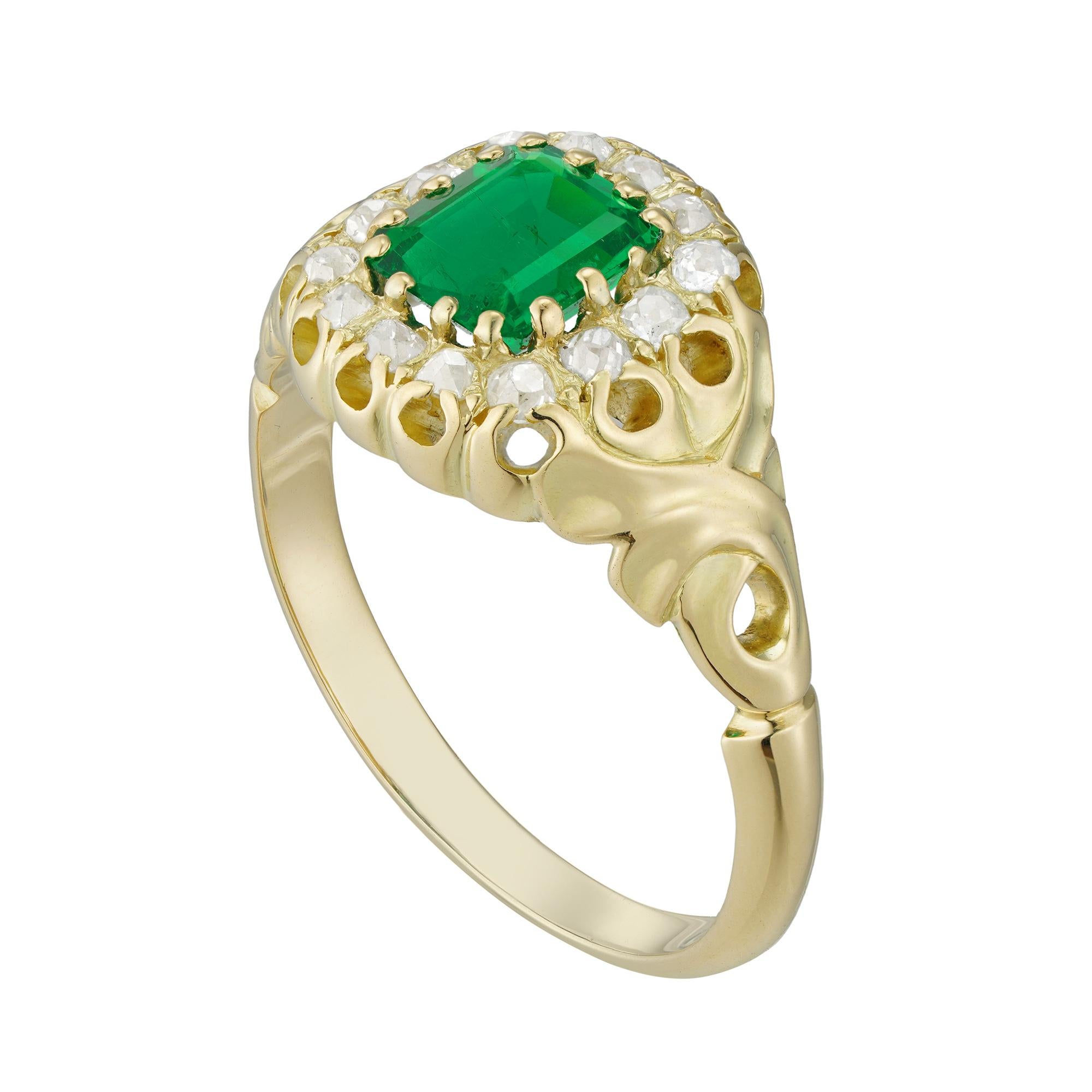 A Late Victorian emerald and diamond cluster ring, the octagonal-cut emerald weighing 0.86 carats, accompanied by GCS Report stating to be of Colombian origin, surrounded by fourteen old European-cut diamonds estimated to weigh 0.5 carats in total,