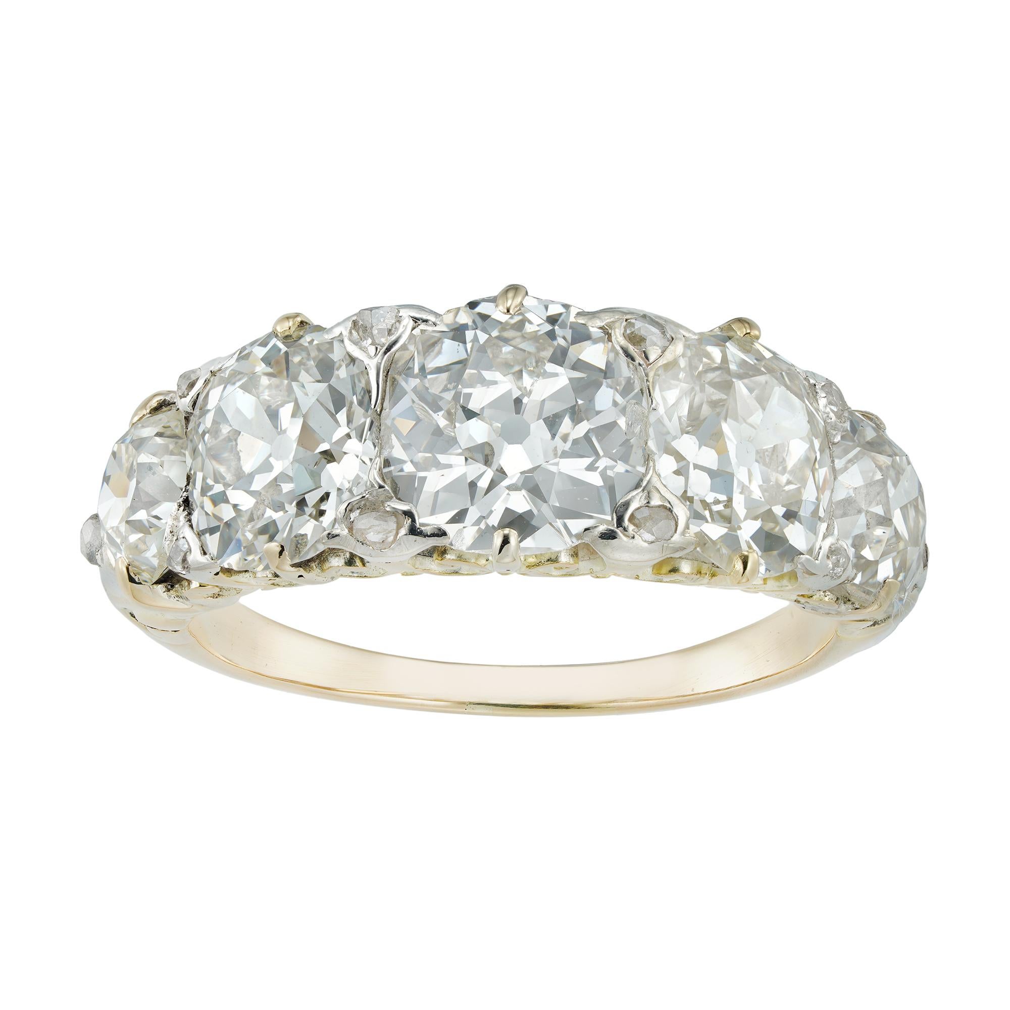 A late Victorian five-stone diamond ring, the five old-cut diamonds graduating from the centre and estimated to weigh 4¾ carats in total, all claw-set with rose-cut diamond in-between, to a silver and yellow gold mount, with scroll pierced mount and