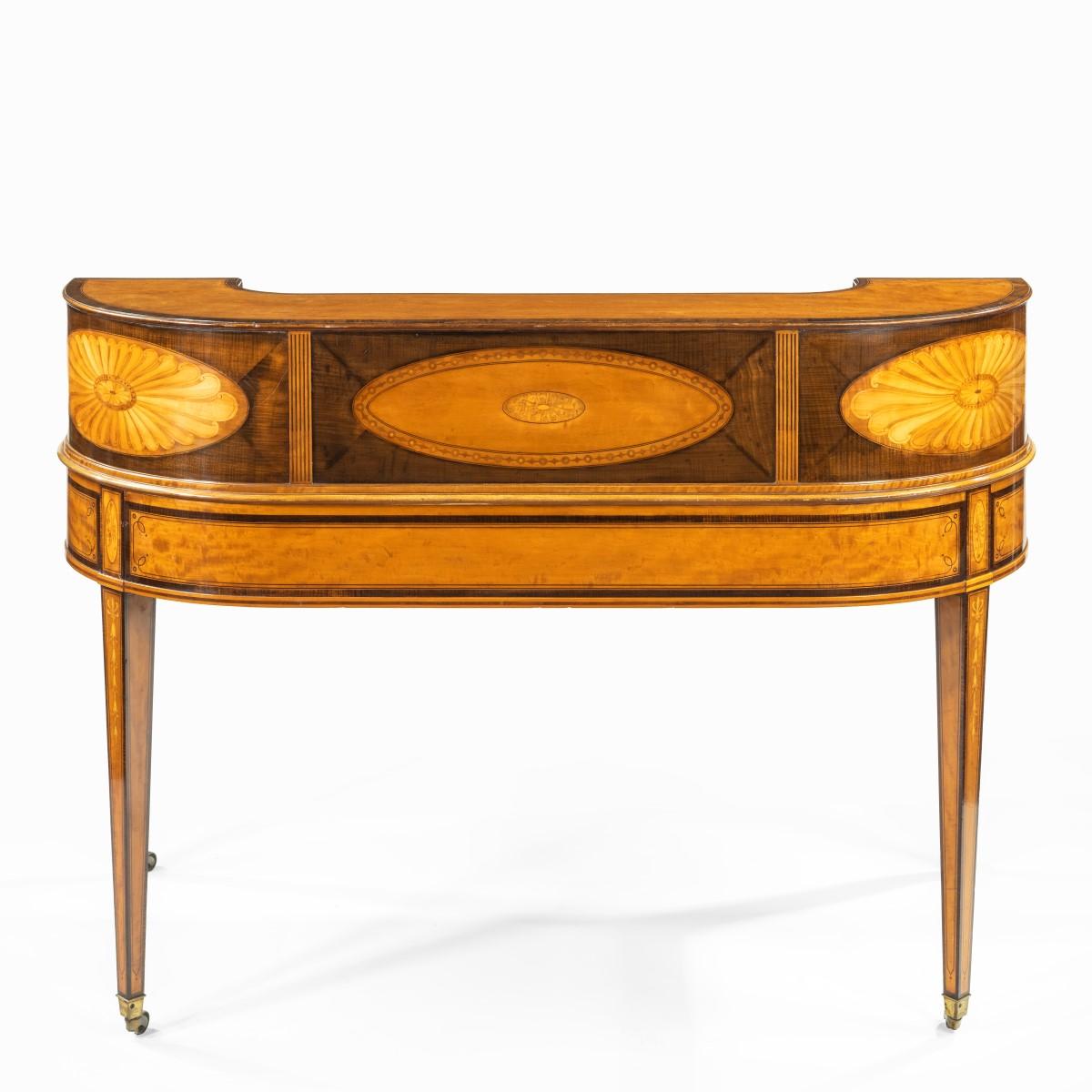 A late Victorian freestanding satinwood Carlton House desk, the curved rectangular top with the typical arrangement of six small drawers and a central cupboard around three sides, enclosing a leathered writing surface, sloping downwards to the