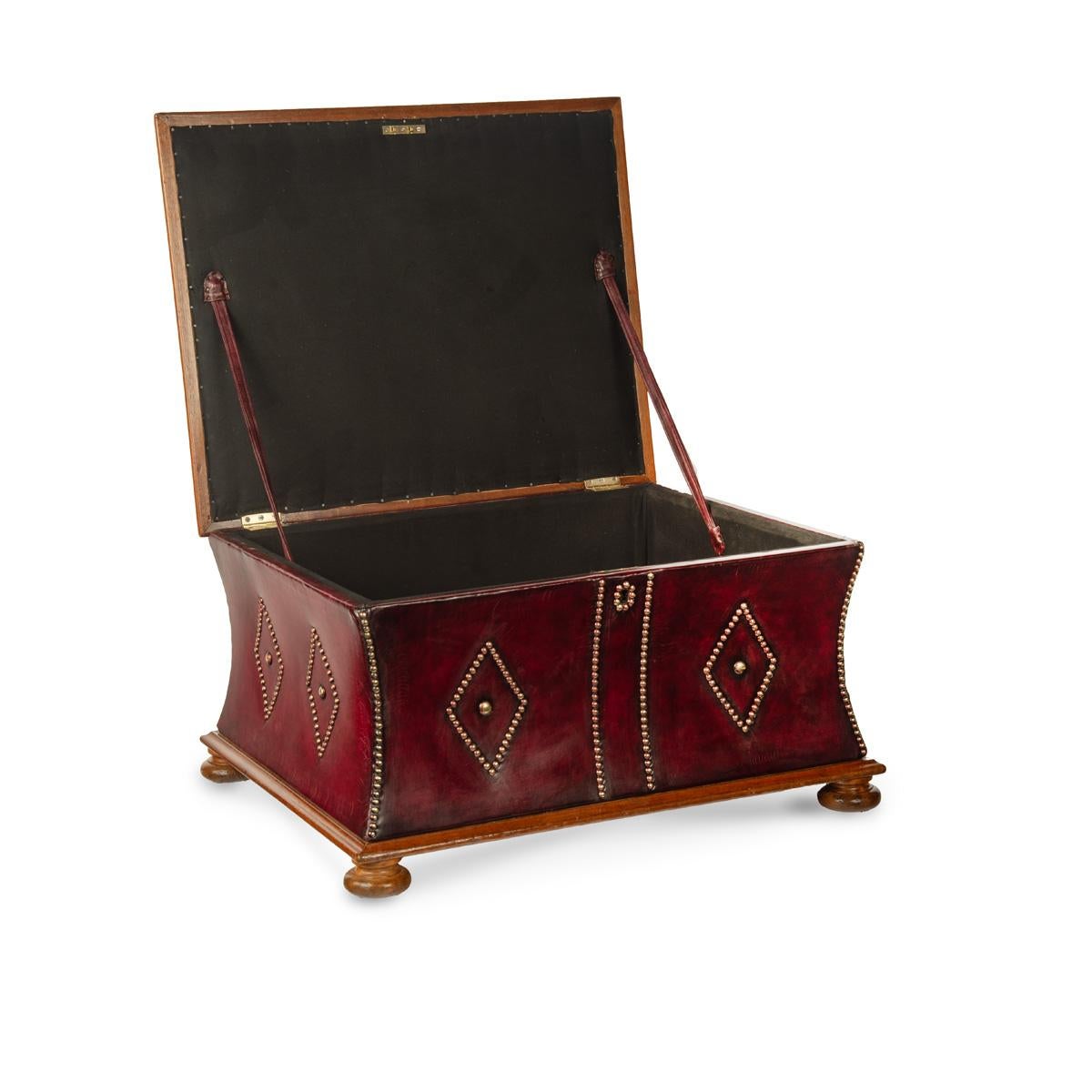 A late Victorian mahogany leathered box stool or Ottoman, of rectangular form, re-upholstered overall in distressed burgundy leather, the hinged lid deep-buttoned to form a seat, the sides decorated with close-nailed brass lozenges and edging, on