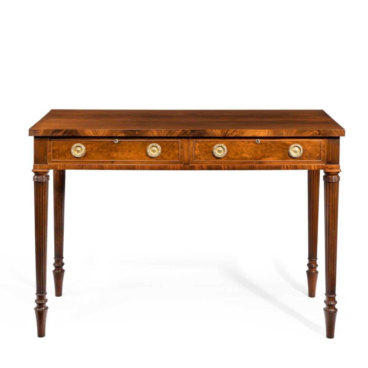 A late Victorian mahogany serving table in the Regency style, the rectangular top with two frieze drawers, set upon tapering reeded legs, the paneled drawer fronts decorated in flame mahogany and with the original ring handles. English, circa 1890.