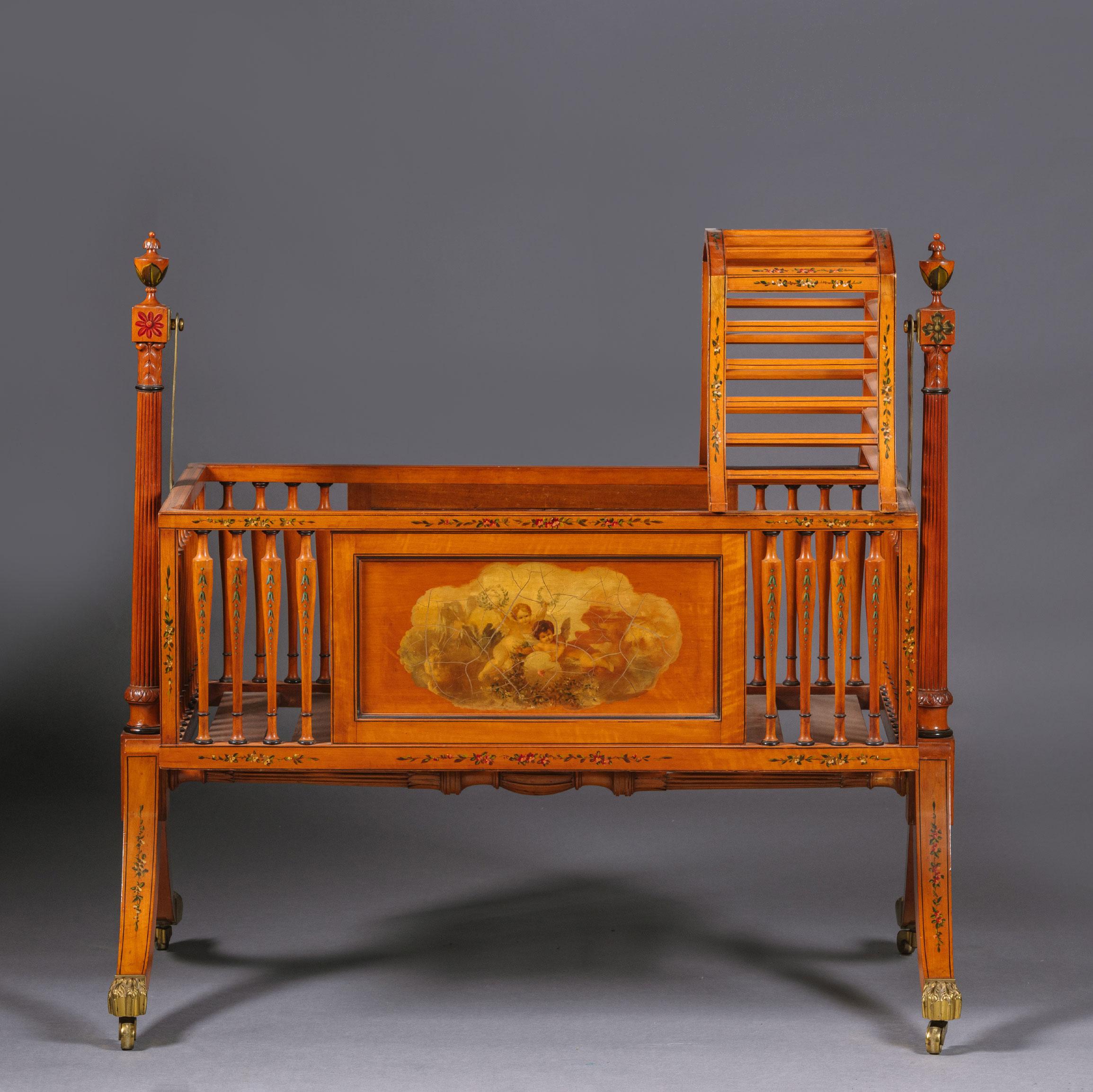 A late Victorian polychrome-decorated satinwood crib. After a Design by Thomas Sheraton. 

Made from precious satinwood decorated with polychrome painted flowers and husk trails. The front and back with 'vernis Martin' scenes of cherubs. The hood