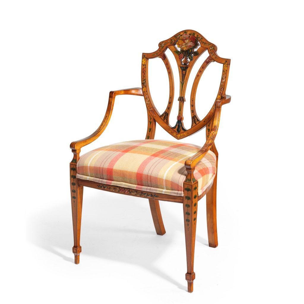 A late Victorian Sheraton revival painted satinwood armchair, the shield shaped back and curved arms set upon square tapering front legs and outswept back legs, painted in polychrome with a central rose and floral garlands, reupholstered. English,