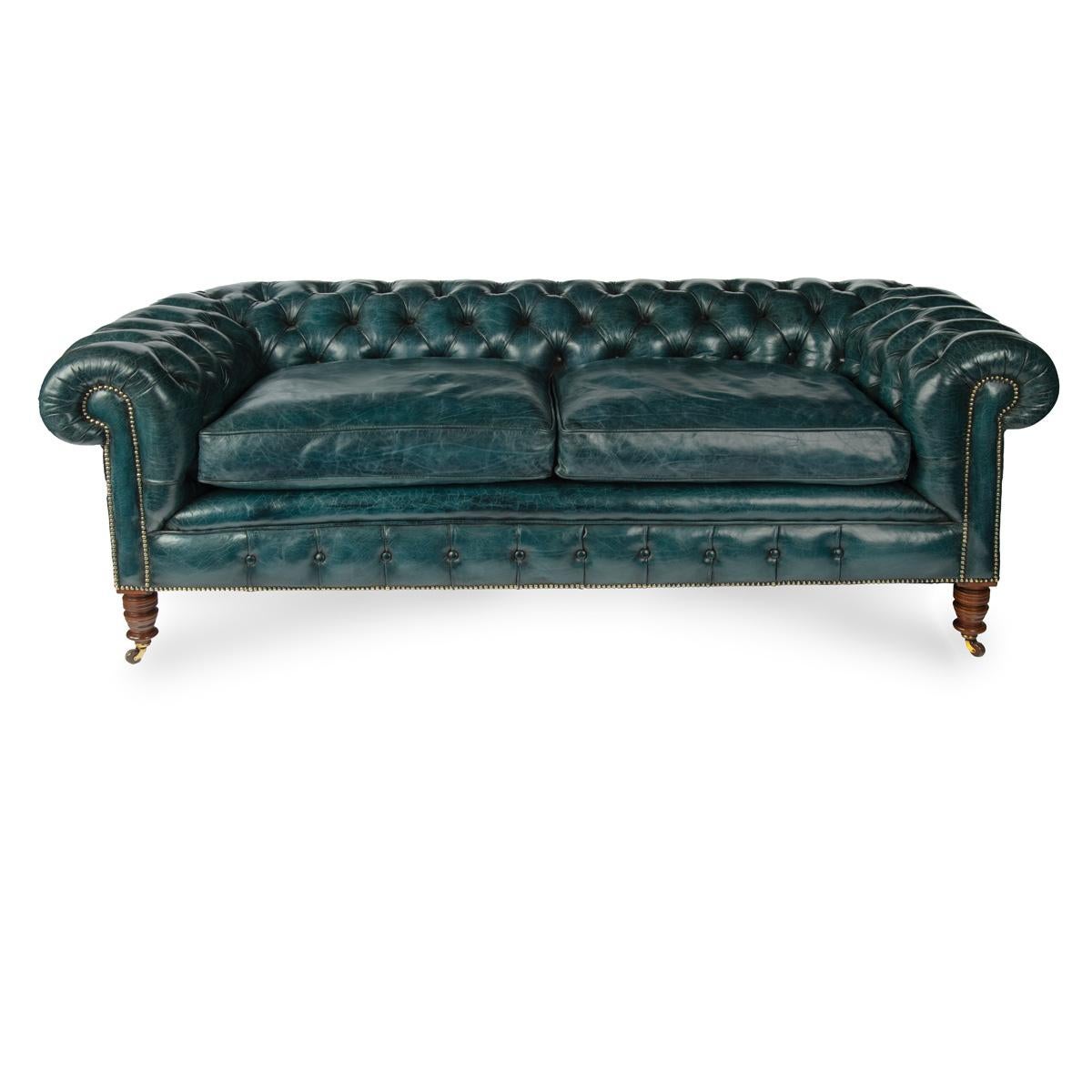 A late Victorian two-seater Chesterfield sofa, of typical form with a continuous scroll back and arms, reupholstered in deep-buttoned blue leather, raised on turned tapering walnut legs with the original castors.  English, circa 1900.

