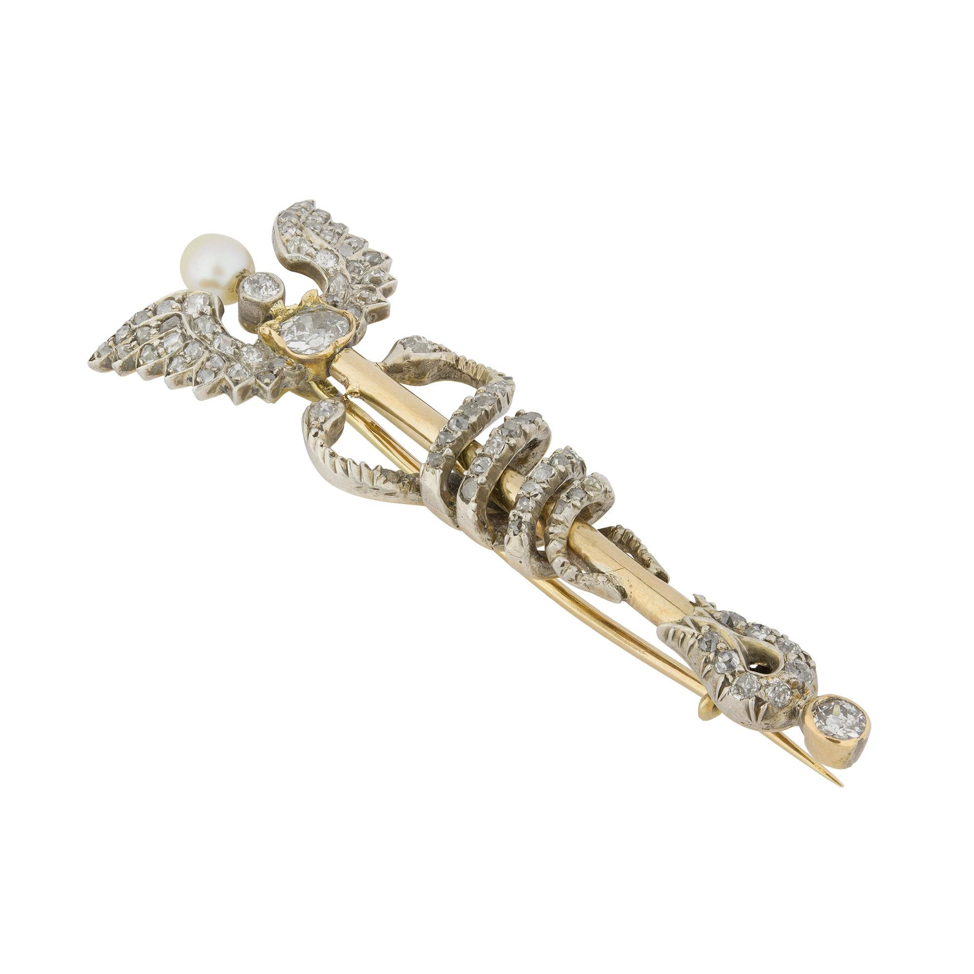 Eine spätviktorianische Caduceus-Brosche aus Gelbgold und Diamanten, der geflügelte Stab ist durchgehend weiß gekrallt und mit alten Diamanten im Brillant- und Rosenschliff besetzt, in der Mitte befindet sich eine natürliche Perle, zwei