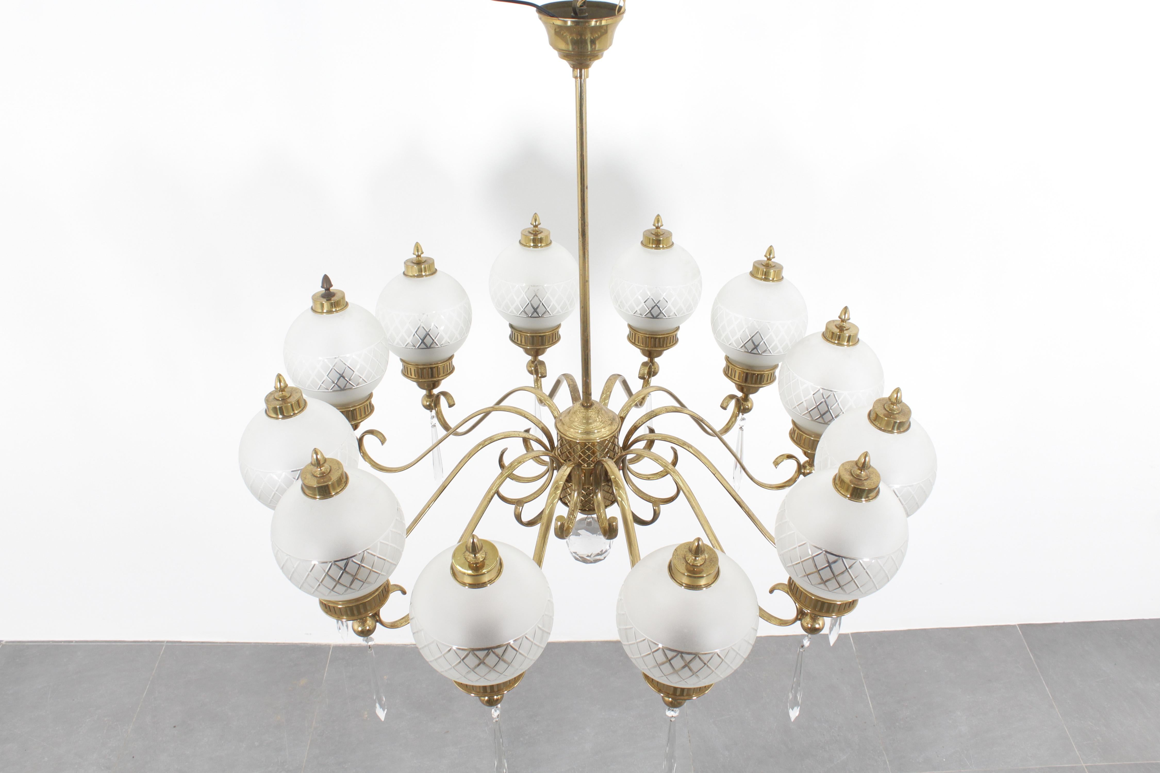 Imponente e scultoreo lampadario a 10 bracci in ottone curvato con diffusori a globo in vetro satinato lavorato e finiture in ottone con elementi pendenti in cristallo sfaccettato. Disegnato da Angelo Lelii per Arteluce, produzione italiana degli