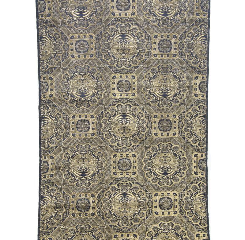 This opulent gold thread and silk cloth has a repeating design of octagonal and square panels enclosing confronting phoenix and flowerheads on a densely patterned geometric ground.  The bolt is wrapped in brown paper secured with ‘Tate and Lyle Ltd
