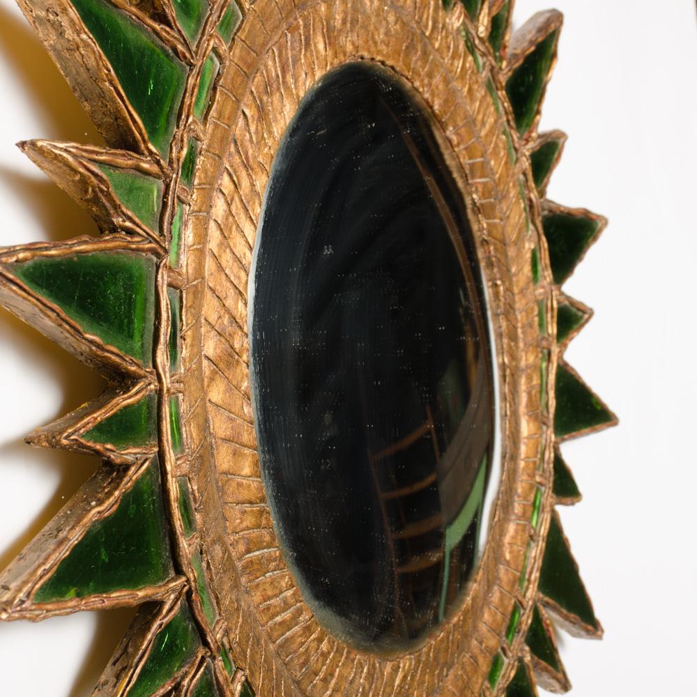A sunburst form mirror having a gilt wood and resin frame with green glass and a central convex mirror. The mirror is made in South America by an artist exclusively for Showrooms 2220.