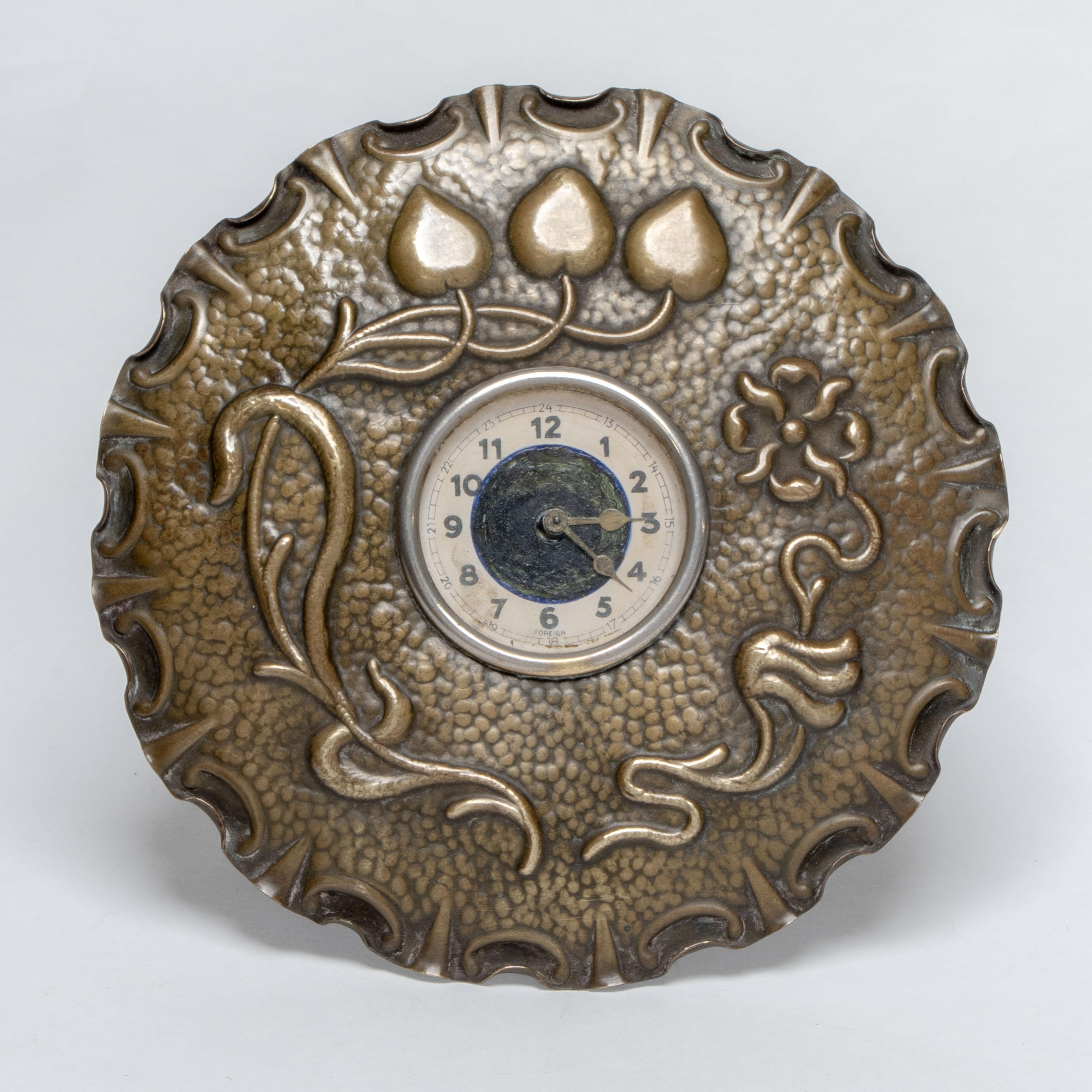 A little Arts and Crafts copper table clock in the shape of a flower head with hand hammered floral decoration, retaining the original simple clock movement which ticks away sweetly.