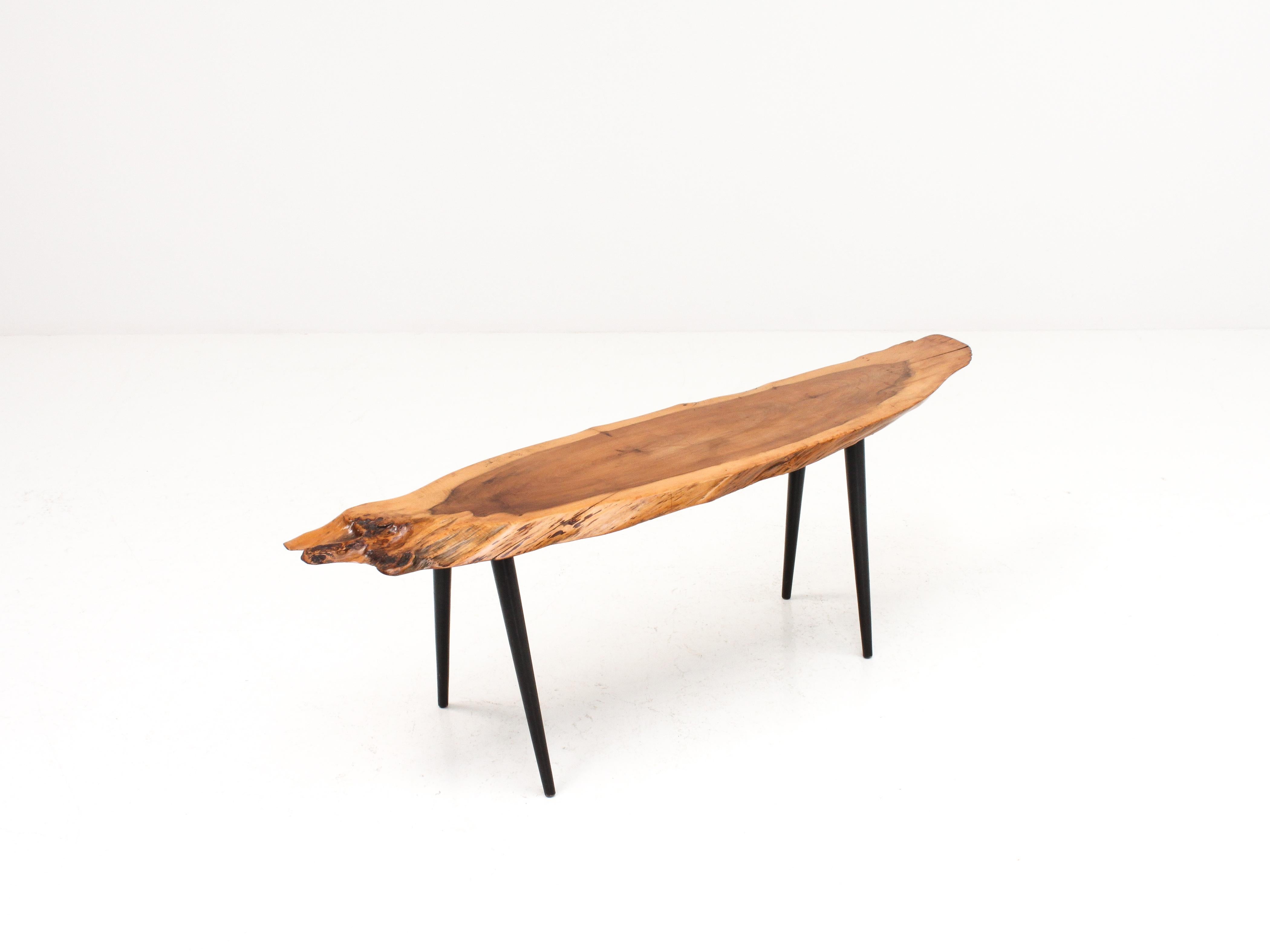 Ein Couchtisch aus den 1960er Jahren mit einer Tischplatte aus massivem Eibenholz, der durch seine organische Ästhetik besticht und auf schrägen, konischen Beinen steht. 

Der Zustand ist insgesamt gut, mit leichten Gebrauchsspuren, wie es sich für
