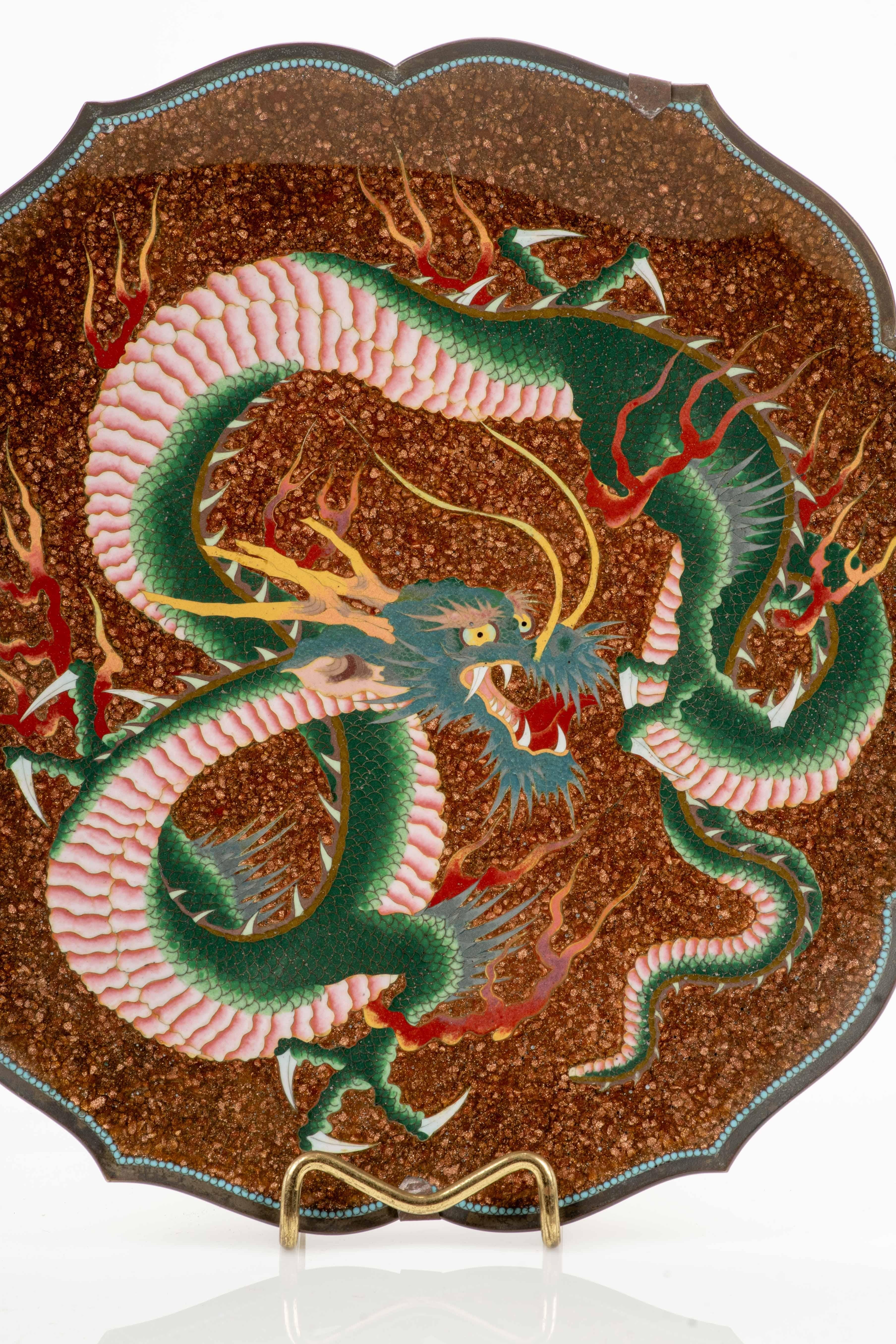 A Japanese cloisonné enamel dish with a lobed rim, decorated with the figure of a Ryu dragon rendered in shaded enamels in tones of green, light blue, pink, and yellow, outlined by fine silver wires.
The aventurine stone ground gives the composition