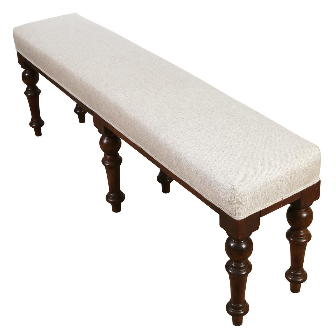 A long English bench with turned mahogany legs, upholstered in a natural linen--perfect for the foot of a bed or in front of the fire.