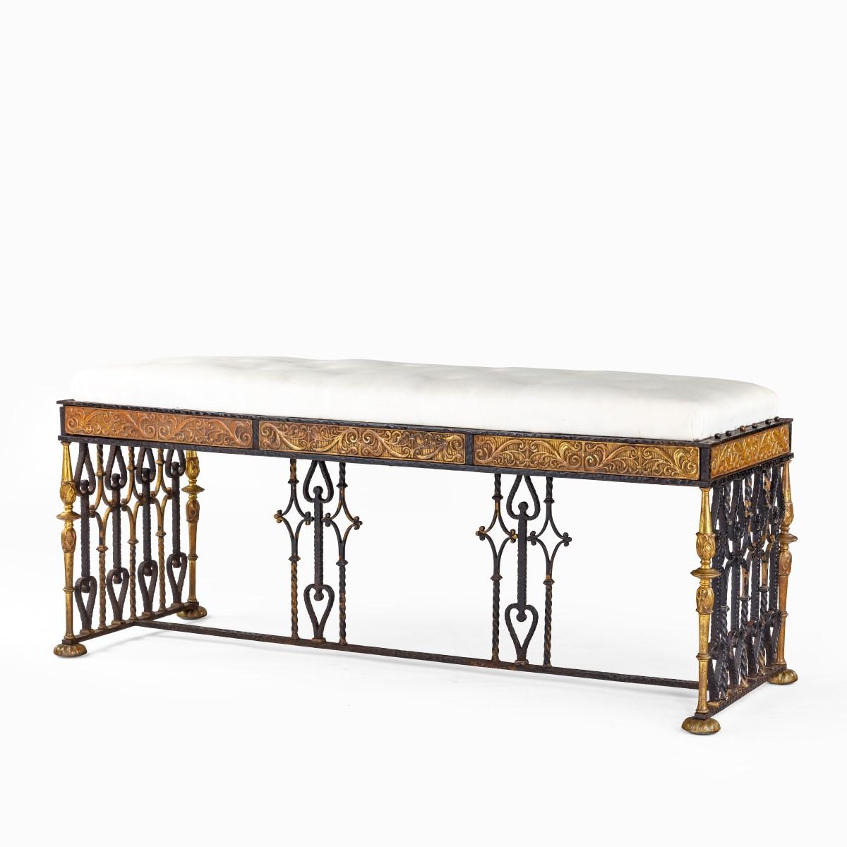 A long parcel gilt wrought iron stool attributed to Oscar Bach, of rectangular form, the openwork diamond- and heart-shaped panels at the ends joined by a single stretcher with two matching supports, the seat rails decorated with ormolu panels of