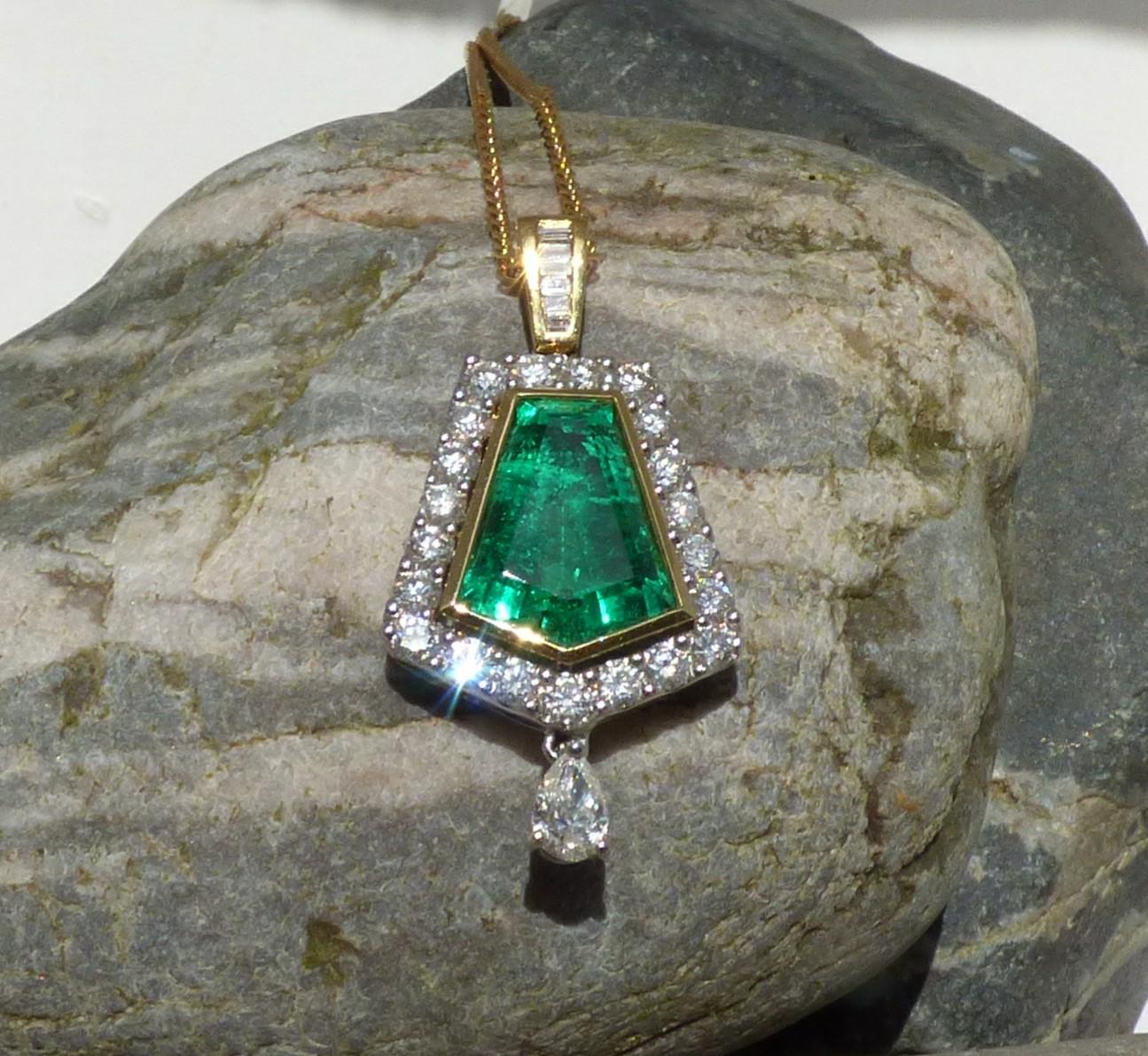 A  colourful and bright natural pentagnoal cut Emerald 13X10mm (4.5ct) is set with 21 round Diamonds (1.13ct), a pear shaped Diamond (.28ct) and six baguette Diamonds (.16ct.). The pendant is handmade in 18K yellow and white gold.  The pendant is
