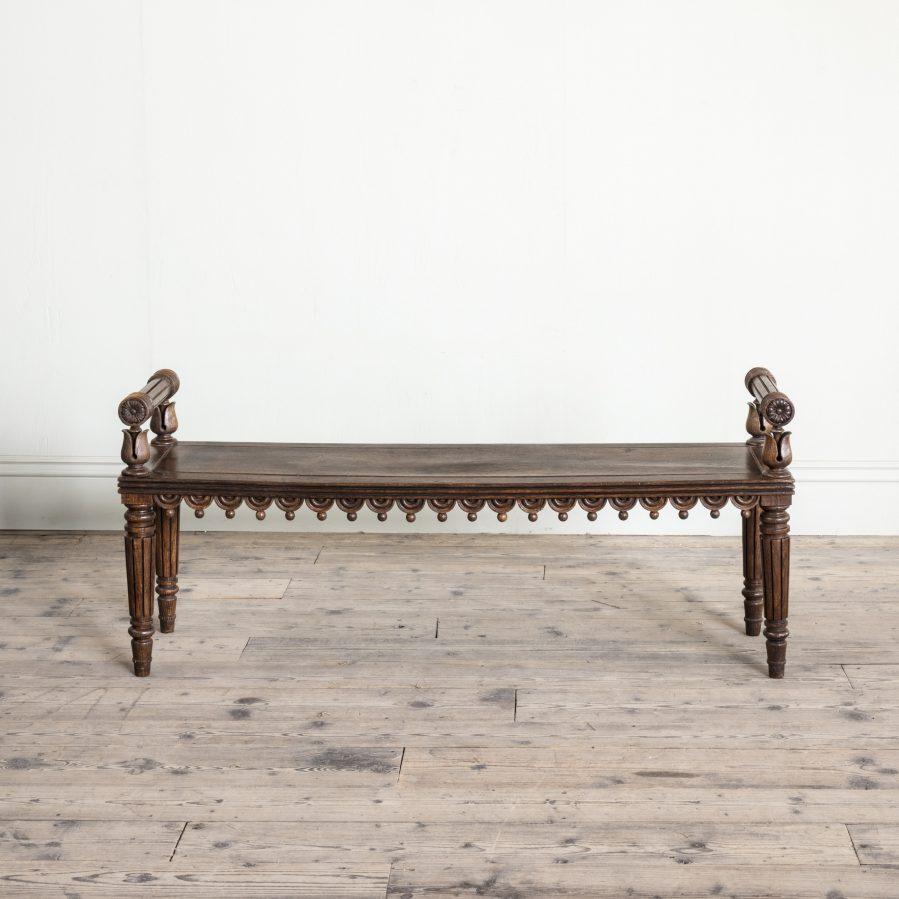 With turned bolster lotus leaf supports, above a panelled seat with a frieze of half roundels and ball pendants, on turned fluted legs, circa 1815.