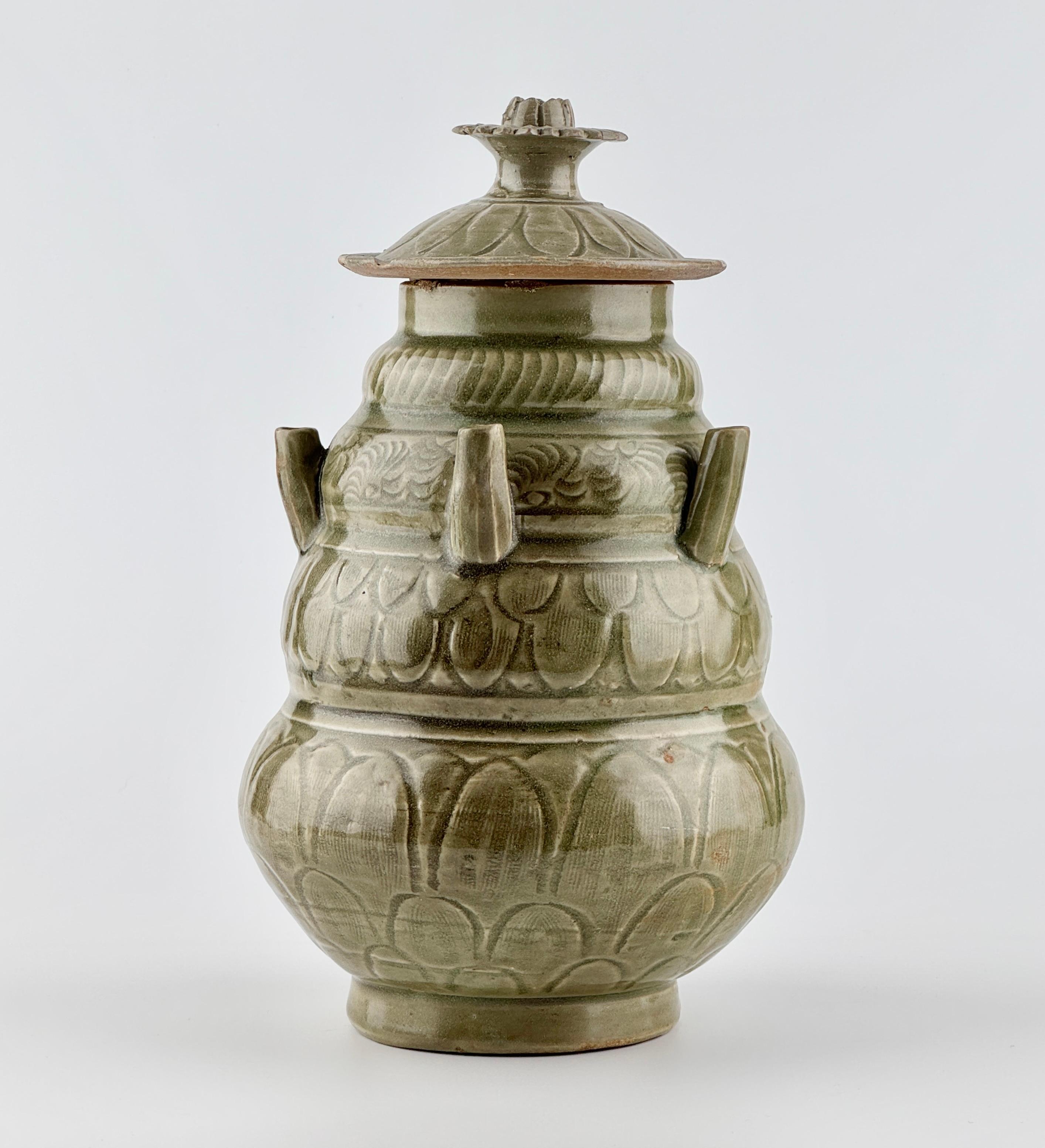 The jar features a round body with well-proportioned four distinct tiers and a short, stable foot. The surface is coated in a deep green Longquan celadon glaze, showcasing the sprout-like finial on the lid and the detailed carved leaf motifs. Five
