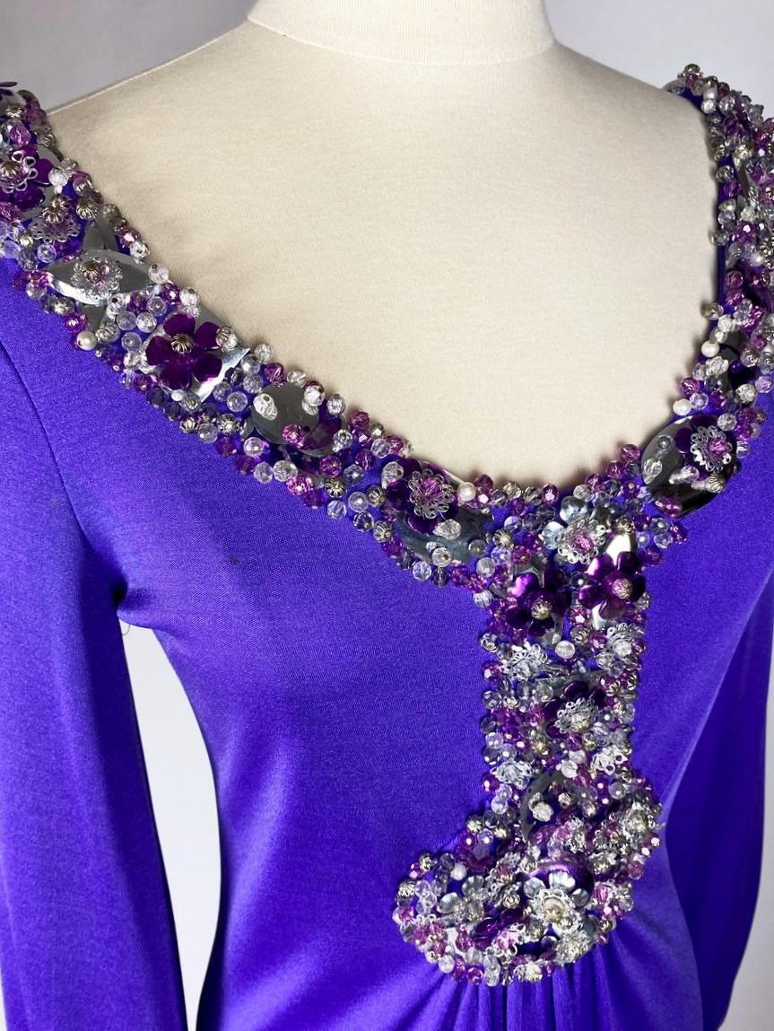 Circa 1970-1975

France

A Jewellery evening dress in purple  lycra jersey by Loris Azzaro Haute Couture dating from the 1970s. Fluid and stretchy dress with large boat neckline and long puffed sleeves. Psychedelic embroidery forming a pendant on