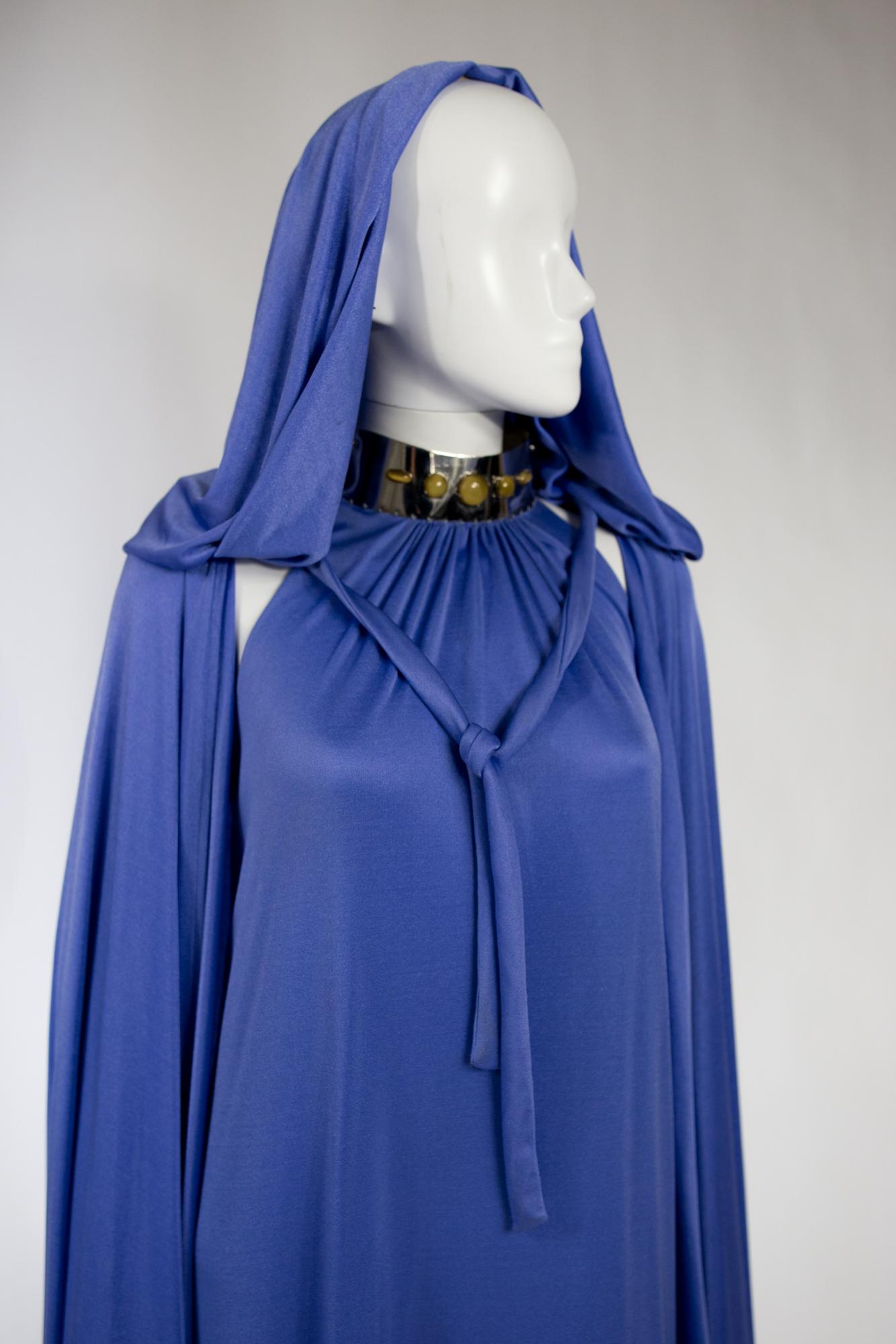Circa 1980/1990

France

Iconic evening set, long dress with dog collar and hooded cape in fluid and stretchy silk jersey from Loris Azzaro Haute Couture. Loose, sleeveless long straight dress, with open shoulders and pleats sewn to an aluminum