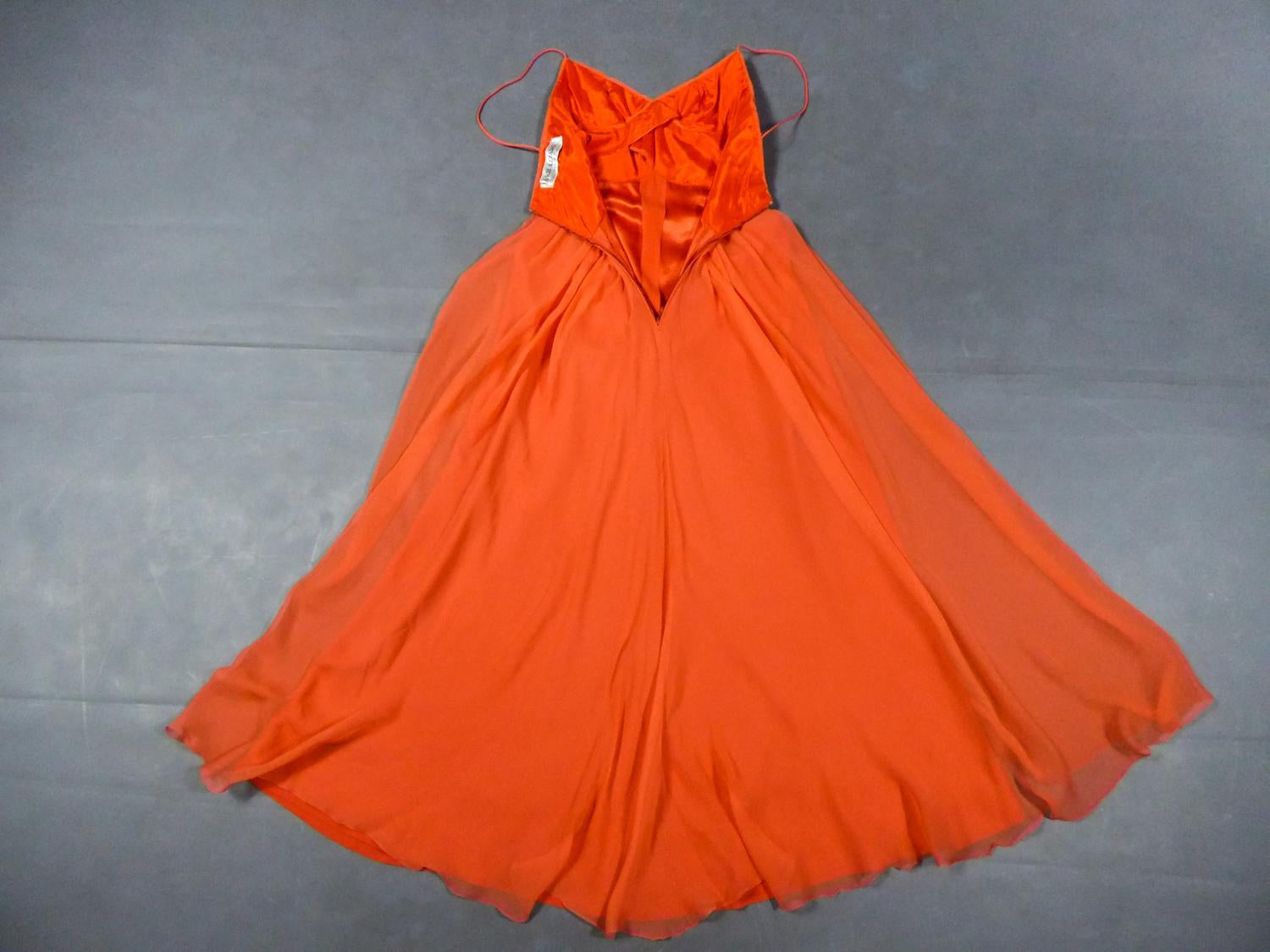 Circa 1980
France

Evening dress in orange silk crepe by Loris Azzaro Haute Couture and dating from the 1990s. Sleeveless dress with thin straps and large cleavage. High-waisted bustier with pleated work by crossed tabs highlighting the chest. Large