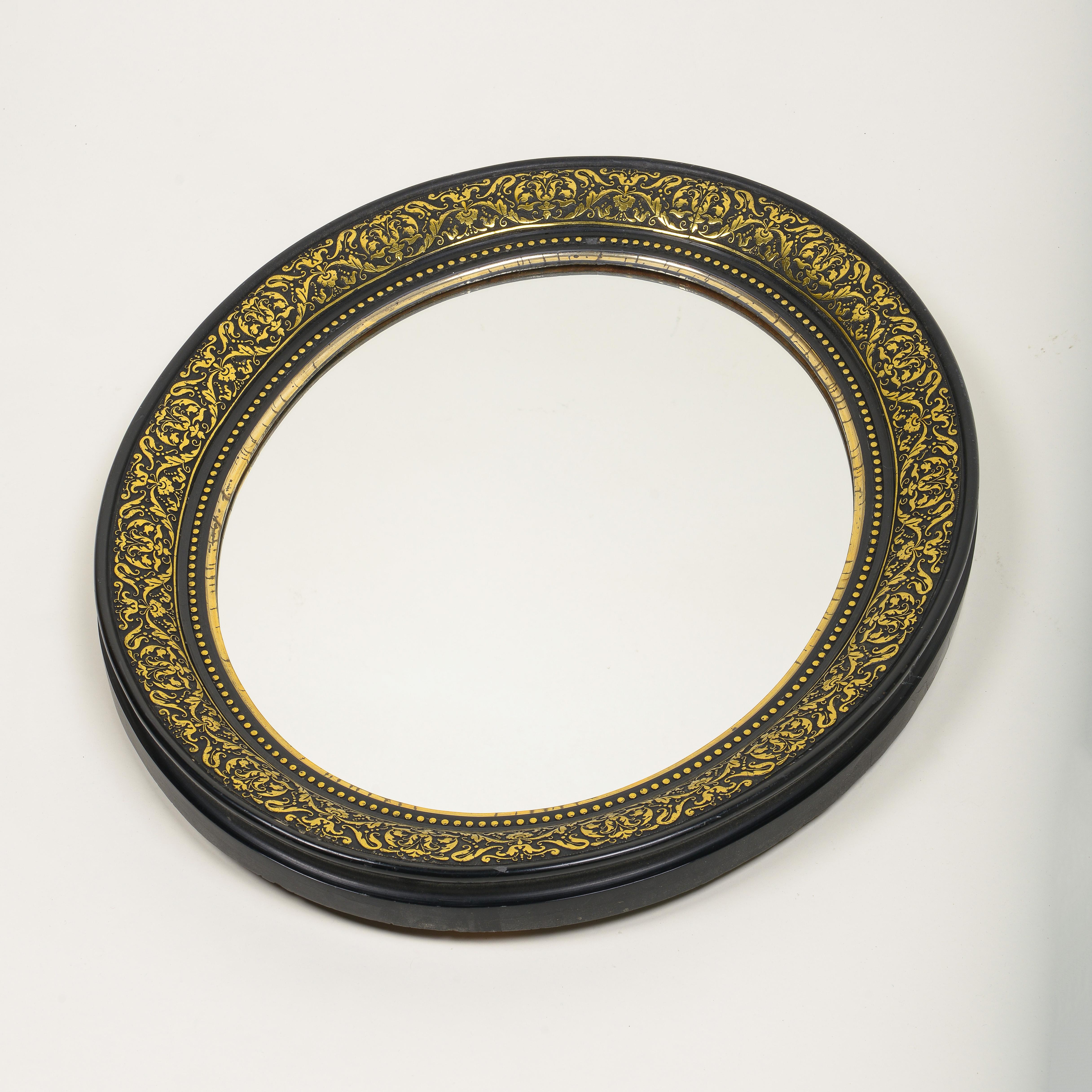 The round mirror plate within a foliate brass repousse inset ebonized wood frame, with gilt and beaded inner slips.
