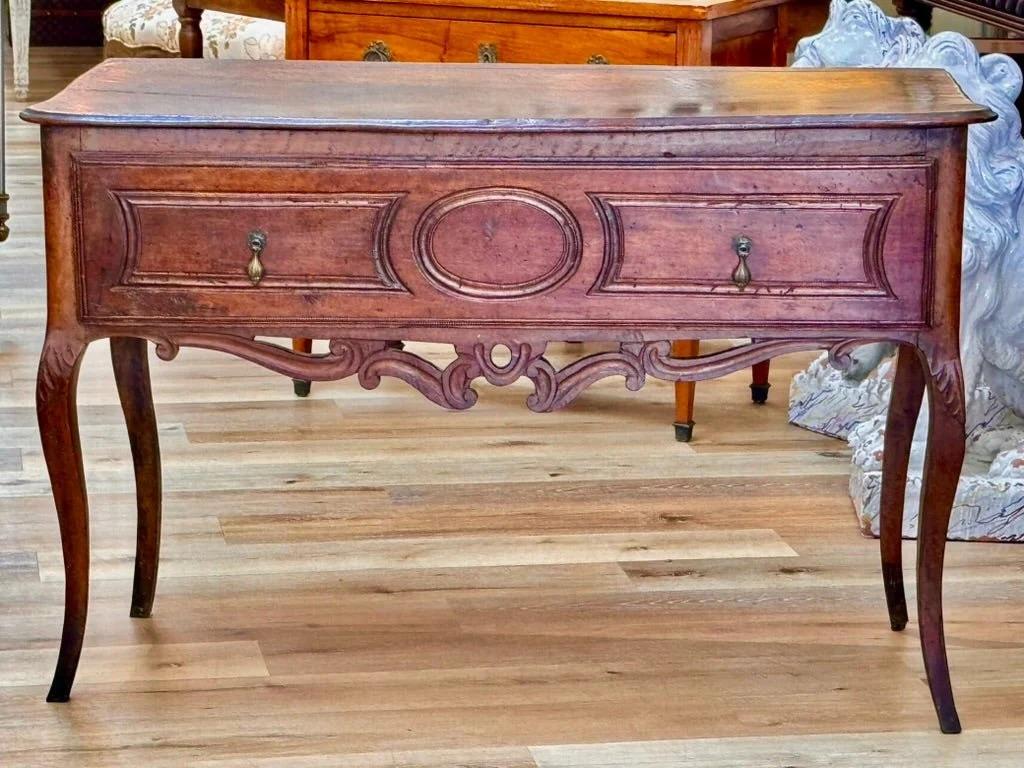 A stunning Louis XV console or side table in richly patinated walnut, featuring a shaped apron with carved scrollwork, cabriole legs, and two paneled drawers flanking a central medallion. Southern France, 18th century. 32.75” h. x 68” w. x 21”

