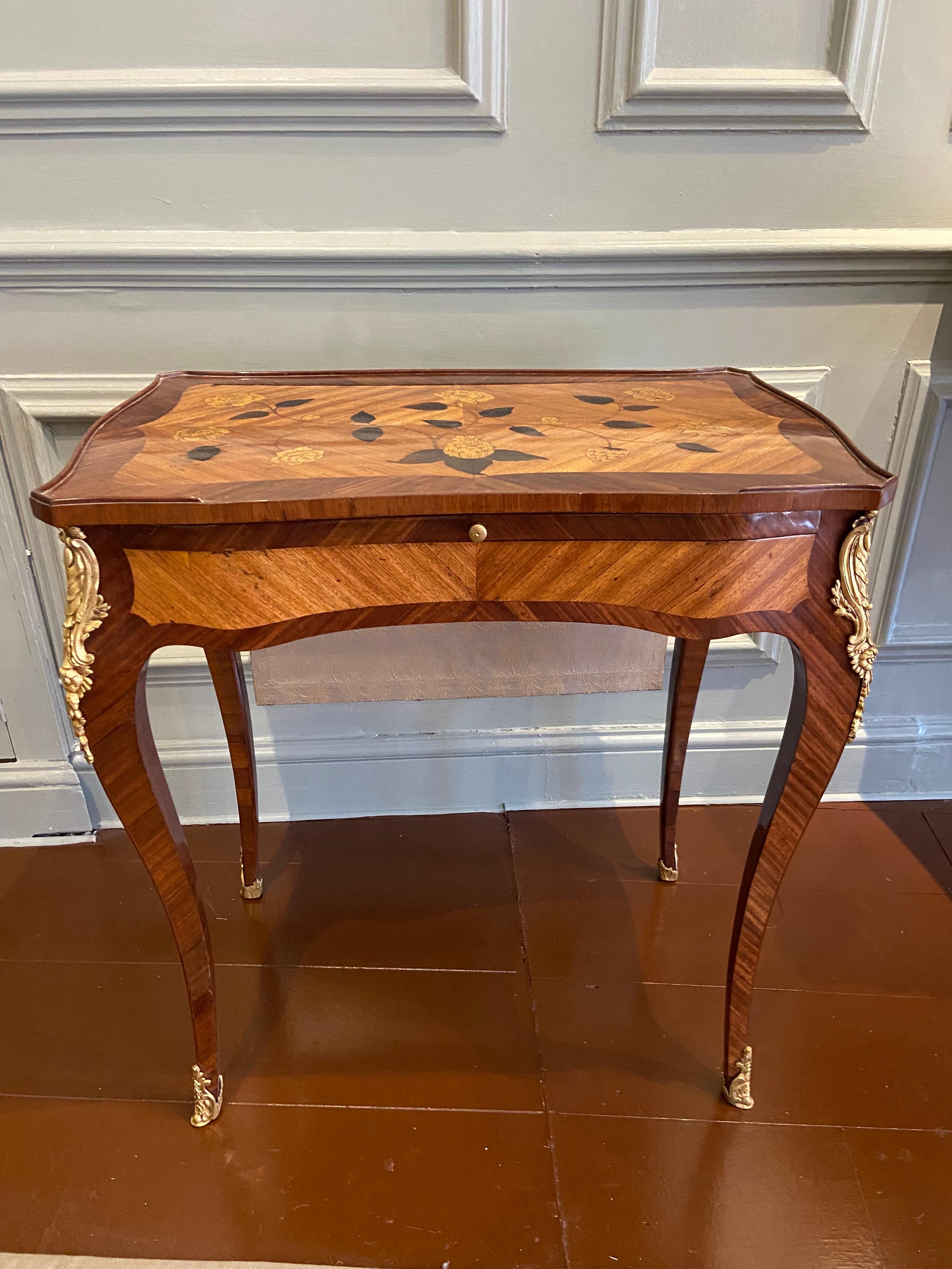 A Louis XV ormolu-mounted bois satine and fruitwood marquetry writing table. Adjustable writing slide with black leather panel, gilt-tooled with central motif; full length drawer with gilt-lock; hidden retractable silk-screen. 

With mark