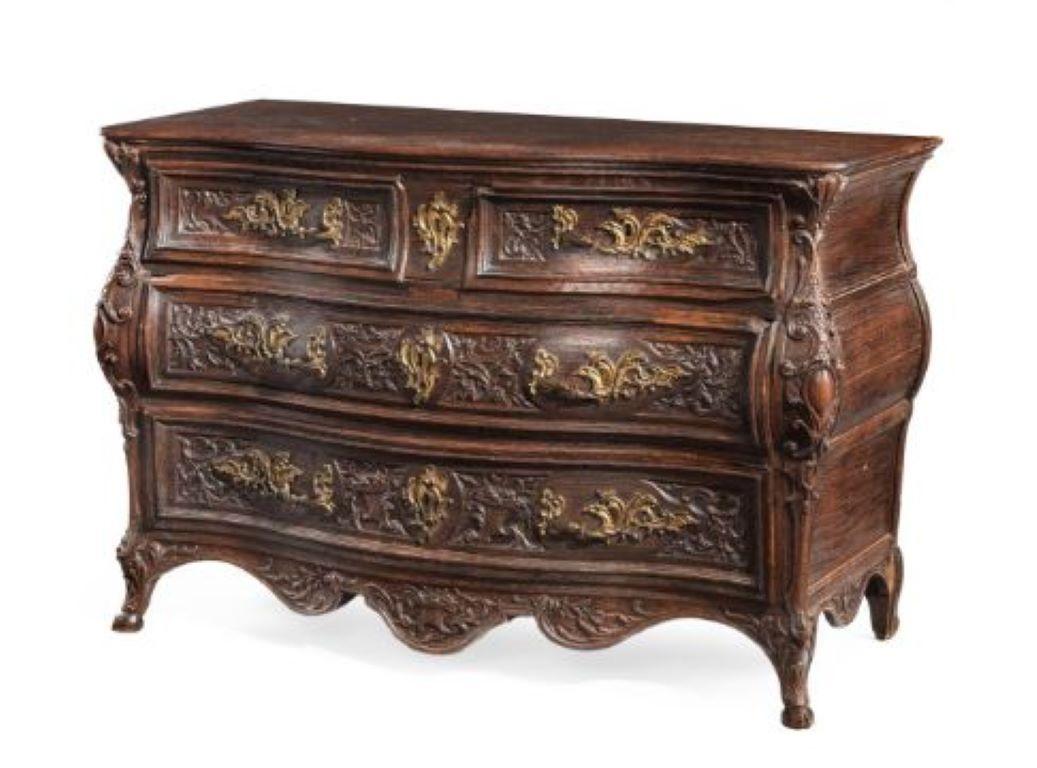 A LOUIS XV BOMBE OAK COMMODE THIRD QUARTER 18TH CENTURY, PROVINCIAL FRANCE With two short and two long panelled drawers carved with foliage, the angles with carved cartouches, handles replaced, 87cm high, 129cm wide, 59cm deep.
