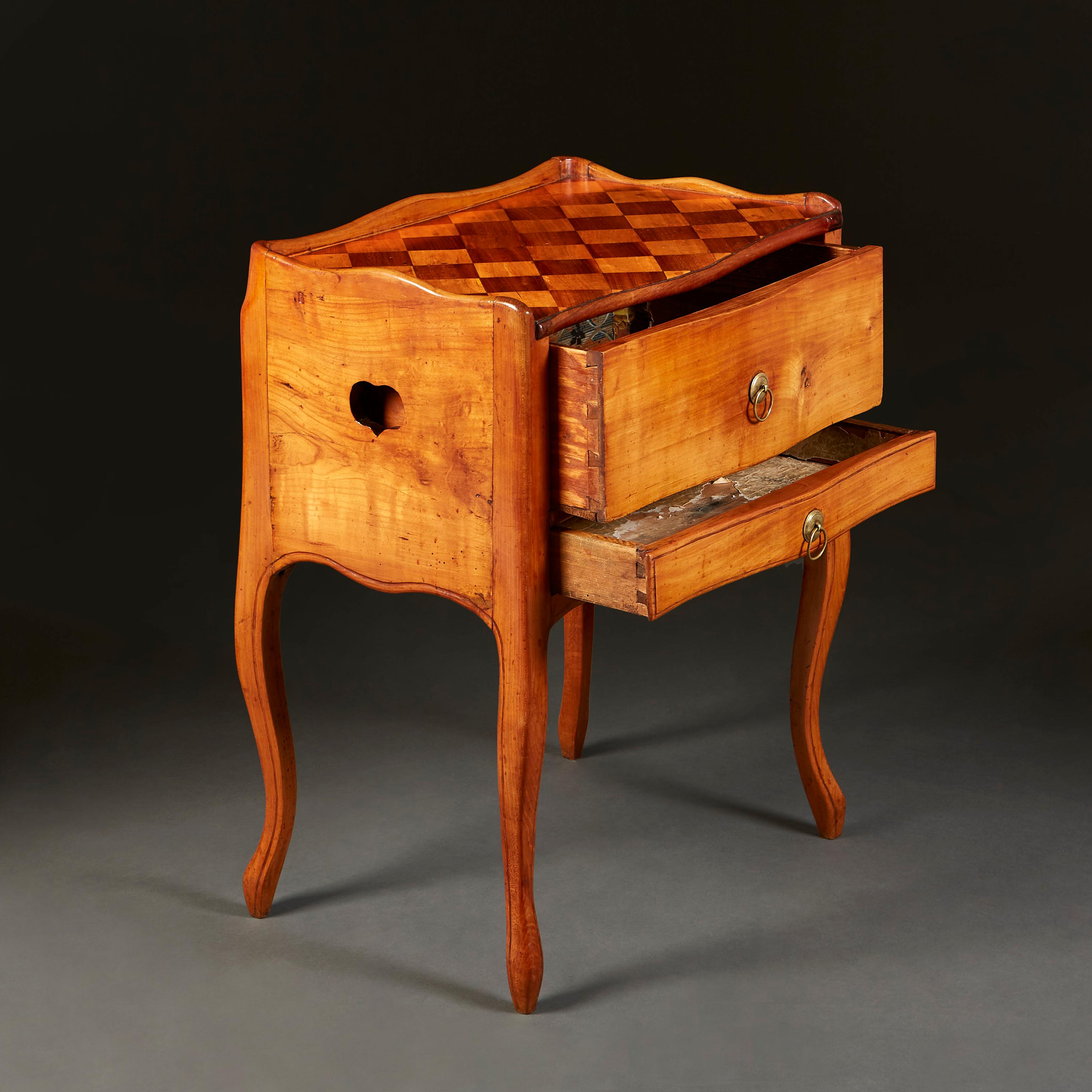 Ein Louis XV Nachttisch aus satiniertem Holz mit zwei Schubladen auf der Vorderseite und herzförmigen Griffen an der Seite. Eine Galerie umgibt die schachbrettartige Intarsienplatte, die auf Kabriolettbeinen mit geformter Schürze steht.
